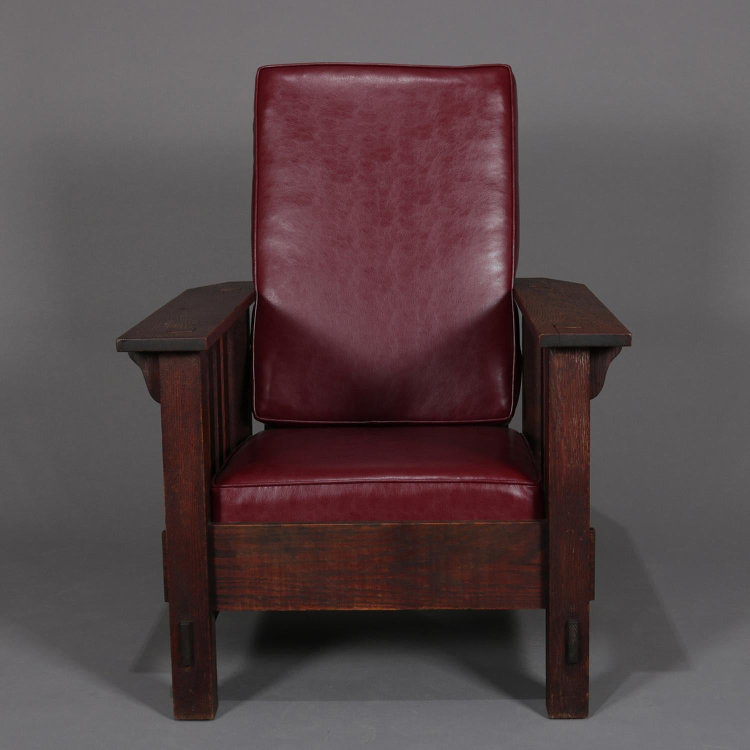 A antique Arts & Crafts Stickley School Morris style chair features oak construction with mortise and tenon joinery, slat sides and back, including faux leather upholstered back and seat cushions, oak Stickley school chair, circa 1910.

Measures: