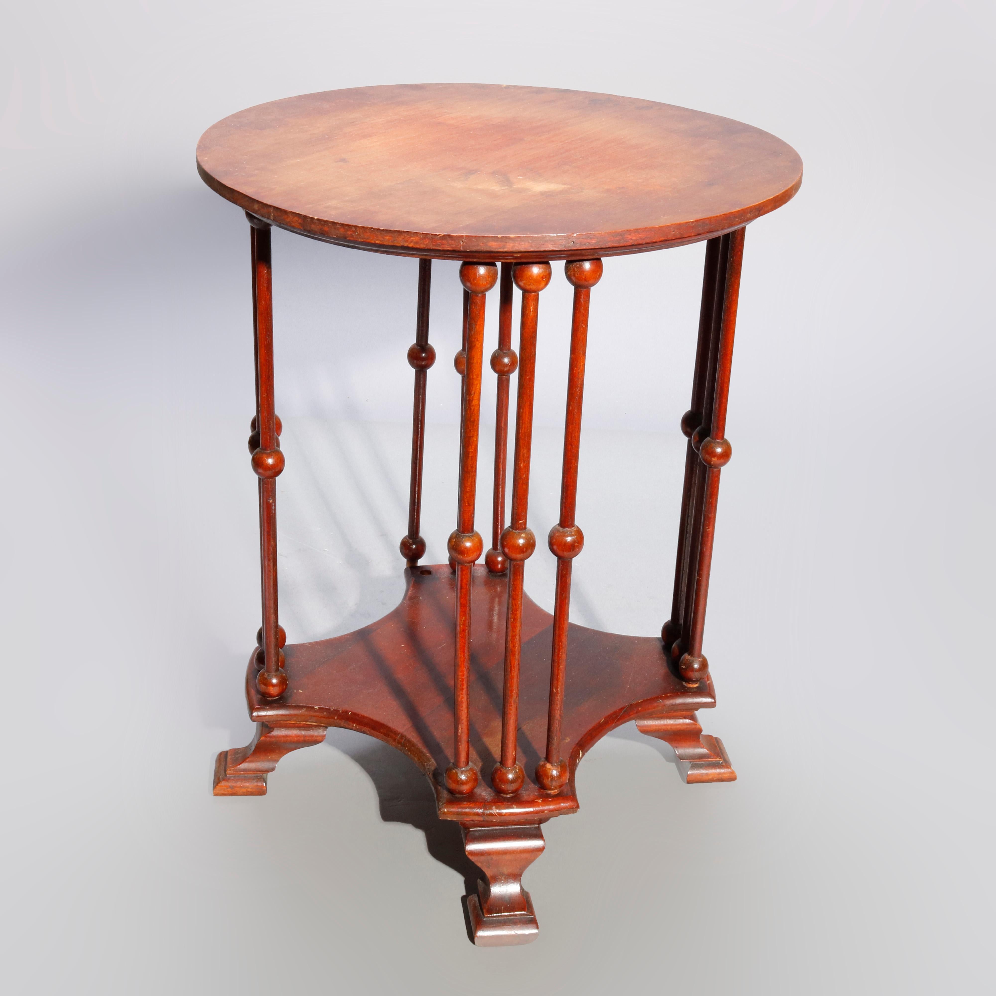 An antique Arts & Crafts style side table offers mahogany construction with round top surmounting stick and ball base having shaped lower shelf and raised on stylized spade feet, 20th century

Measures: 19.25