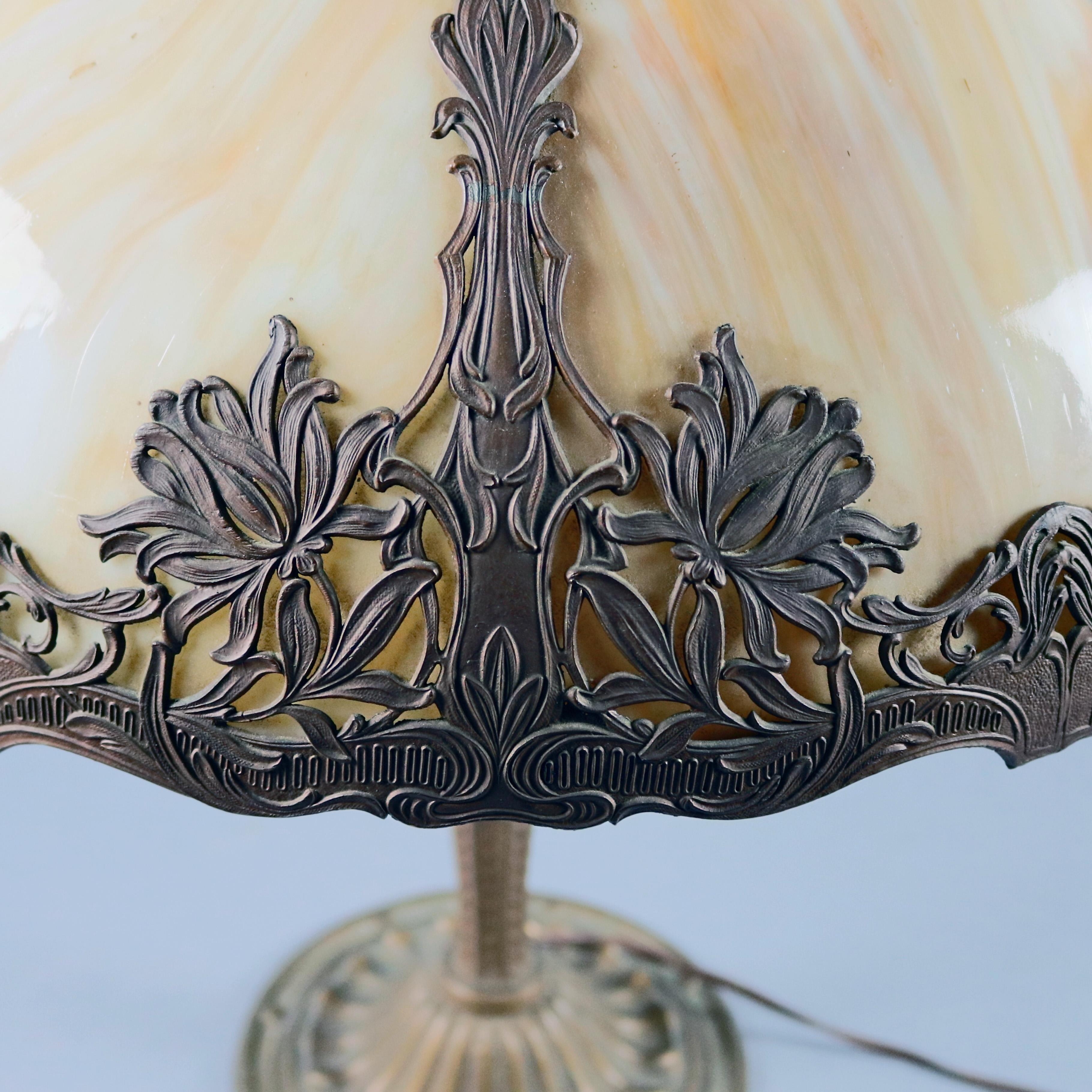 Antique Arts and Crafts era Bradley & Hubbard table lamp features stylized foliate double socket cast base, dome form shade with cast filigree shade having foliate and floral decoration and six bent slag glass panels, transitioning to art Nouveau,