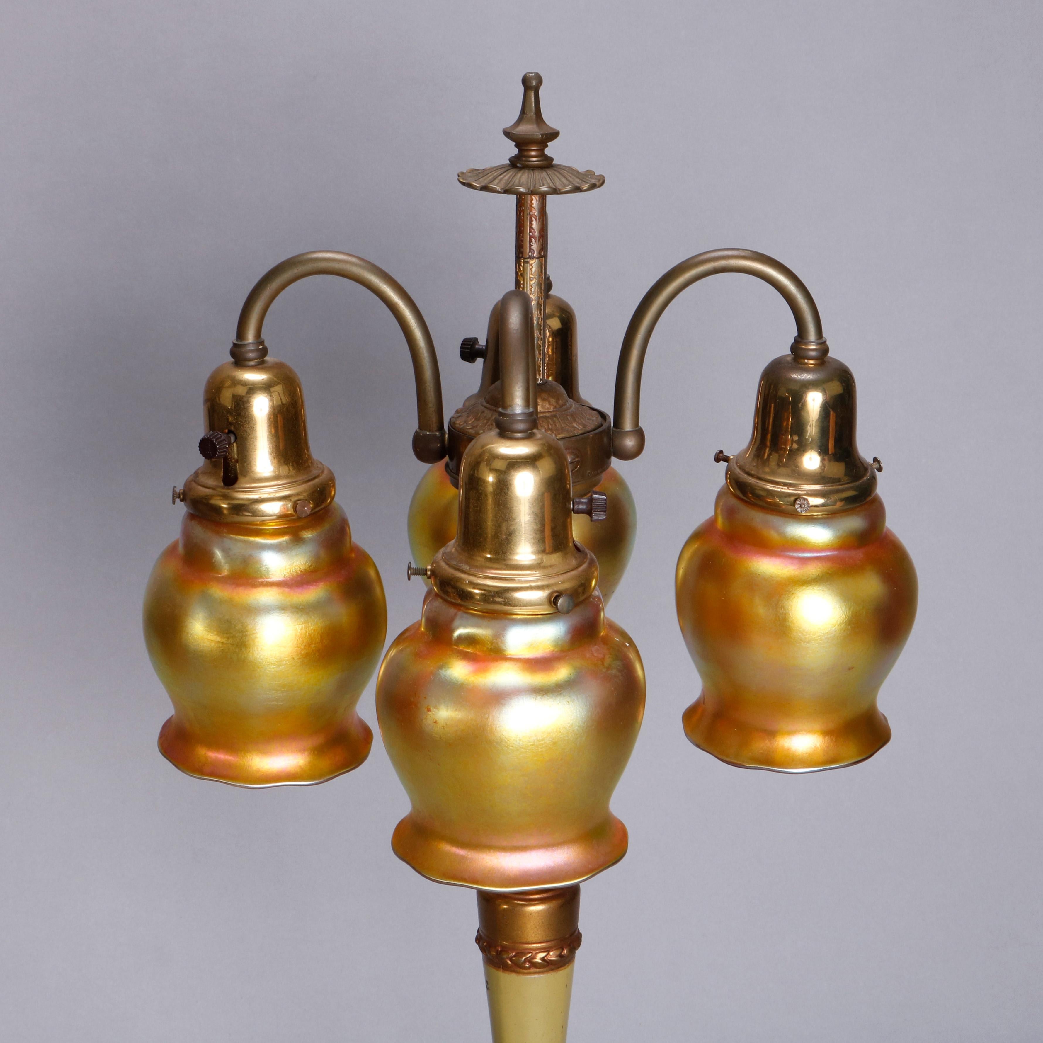 An Arts & Crafts table lamp offers column-form base with acanthus decoration and having four C-scroll arms terminating in gold aurene Steuben art glass tulip form shades, circa 1920

Measures: 25.5