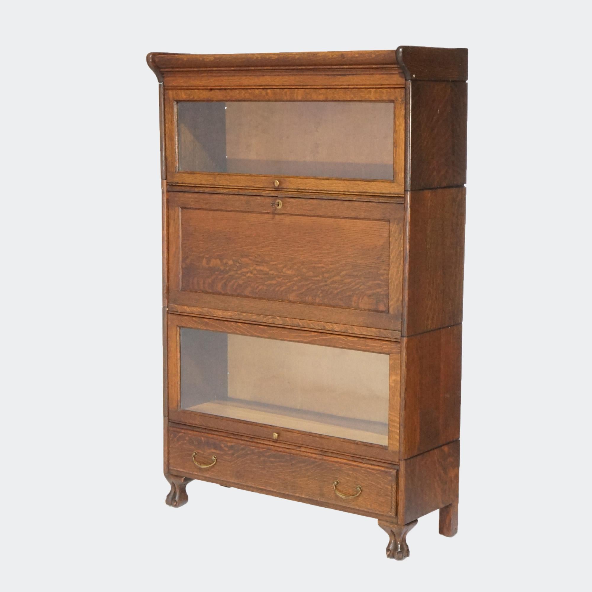 An antique Arts and Crafts barrister bookcase secretary offers quarter sawn oak construction with three stacks; tow having pull-out glass doors and the third with a drop down desk opening to compartmentalized interior; base with single long drawer