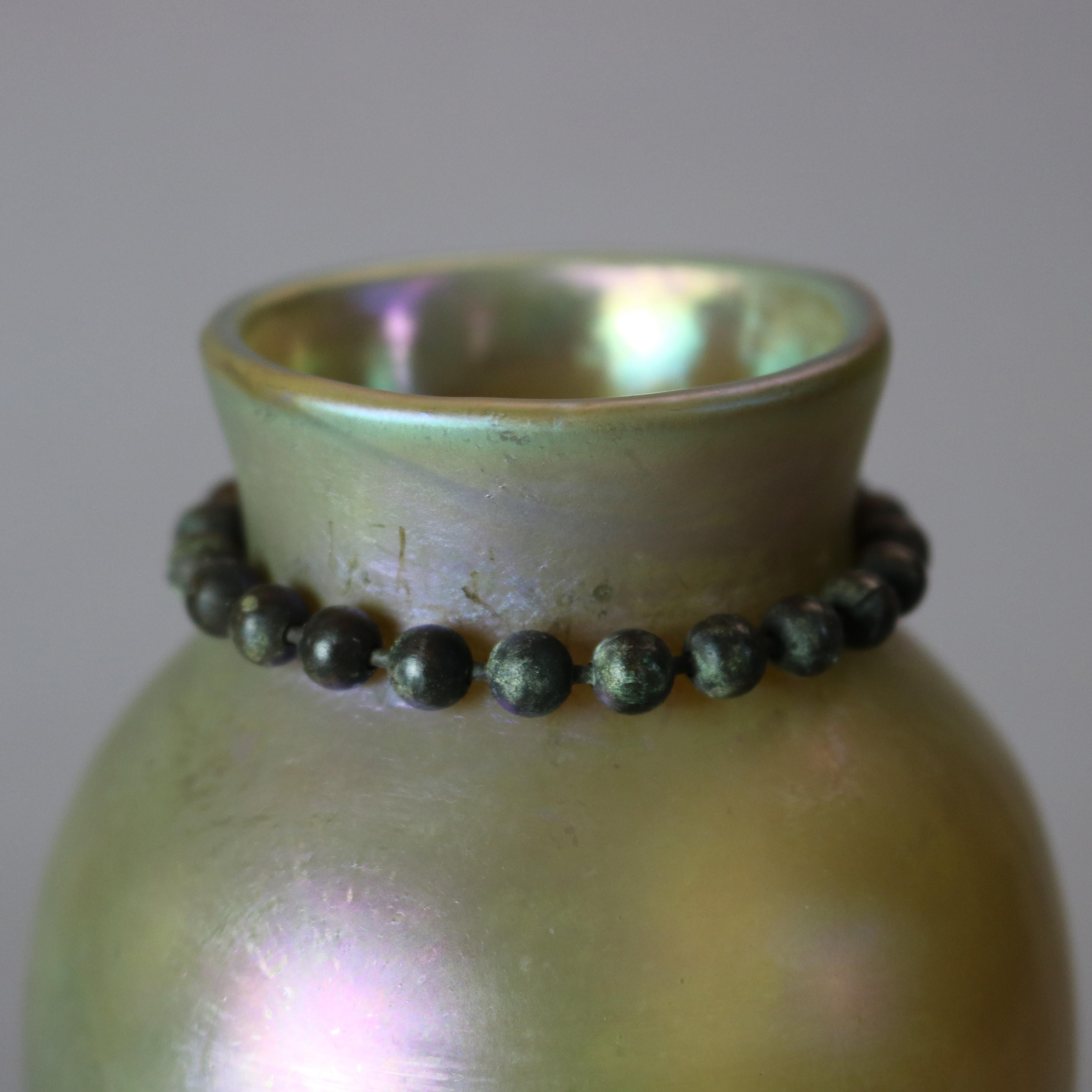 An antique Arts & Crafts vase by Tiffany Studios, New York offers Favrile art glass vessel with bronze bead collar and seated on cast bronze base with beaded collar and incised repeating design, signed on base as photographed, circa
