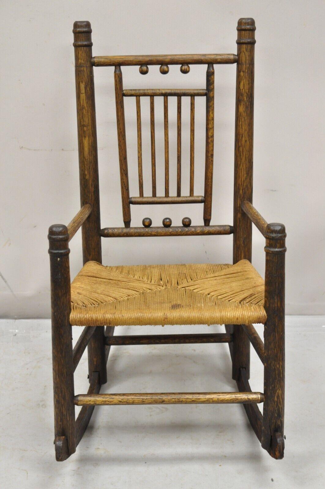 Antique Arts & Crafts Victorian Oak Wood Rush Seat Small Child's Rocking Chair. Item features woven rope cord seat, stick and ball clawed backrest, very unique child's chair.  Circa 19th Century. Measurements: 27