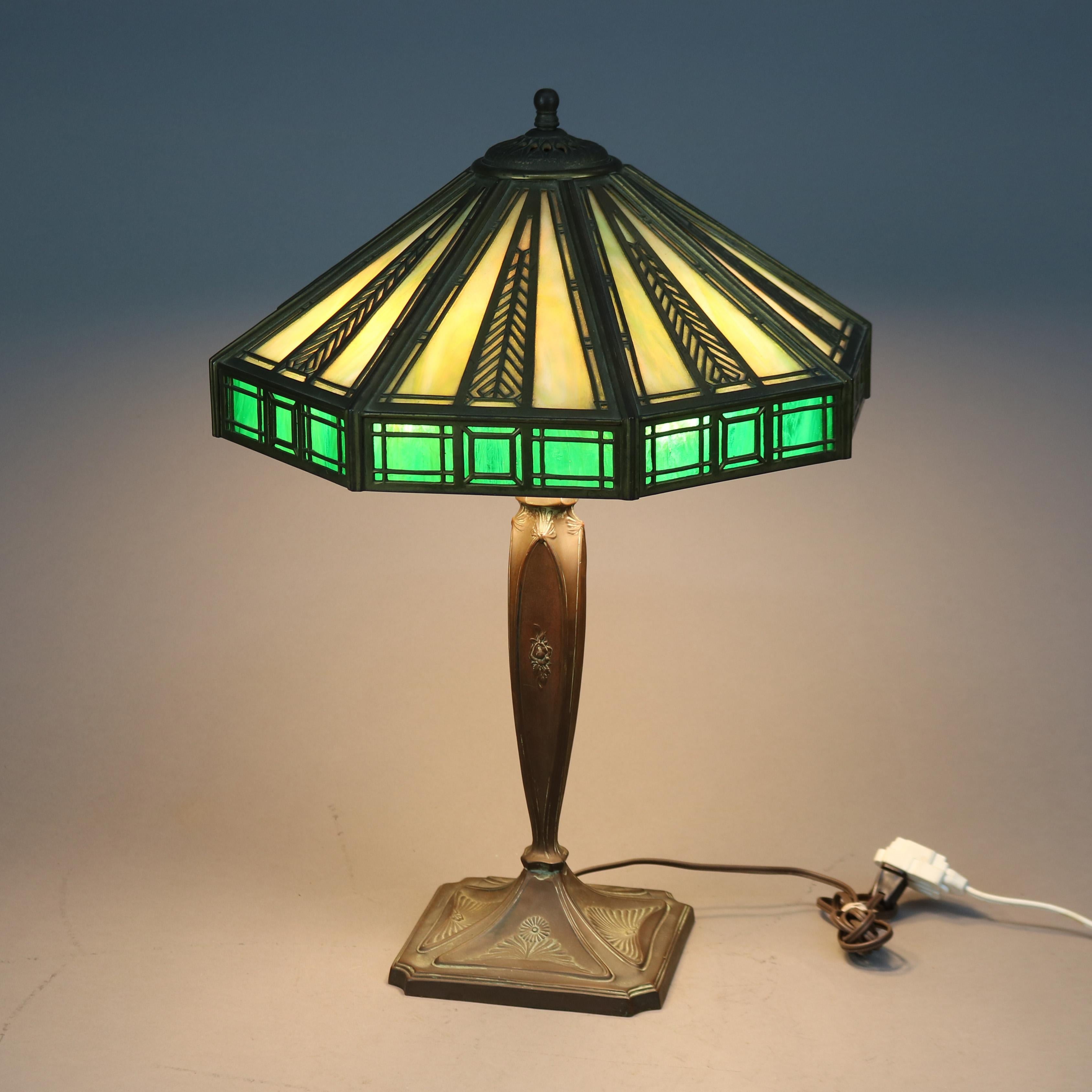 An antique Arts & Crafts table lamp by Wilkinson Lamp Co. offers flared filigree shade having stylized feather pattern and housing two tome slag glass panels over triple socket cast base, maker mark on base as photographed, c1910

Measures -