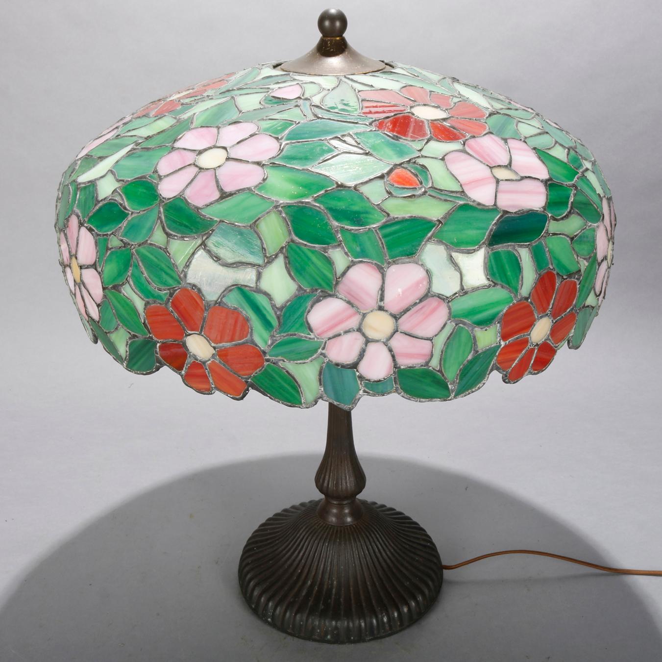 An antique Arts & Crafts leaded glass table lamp in the manner of Williamson offers floral mosaic slag glass shade
surmounting cast base having three independently controlled sockets, circa 1920

Measures: 23.5