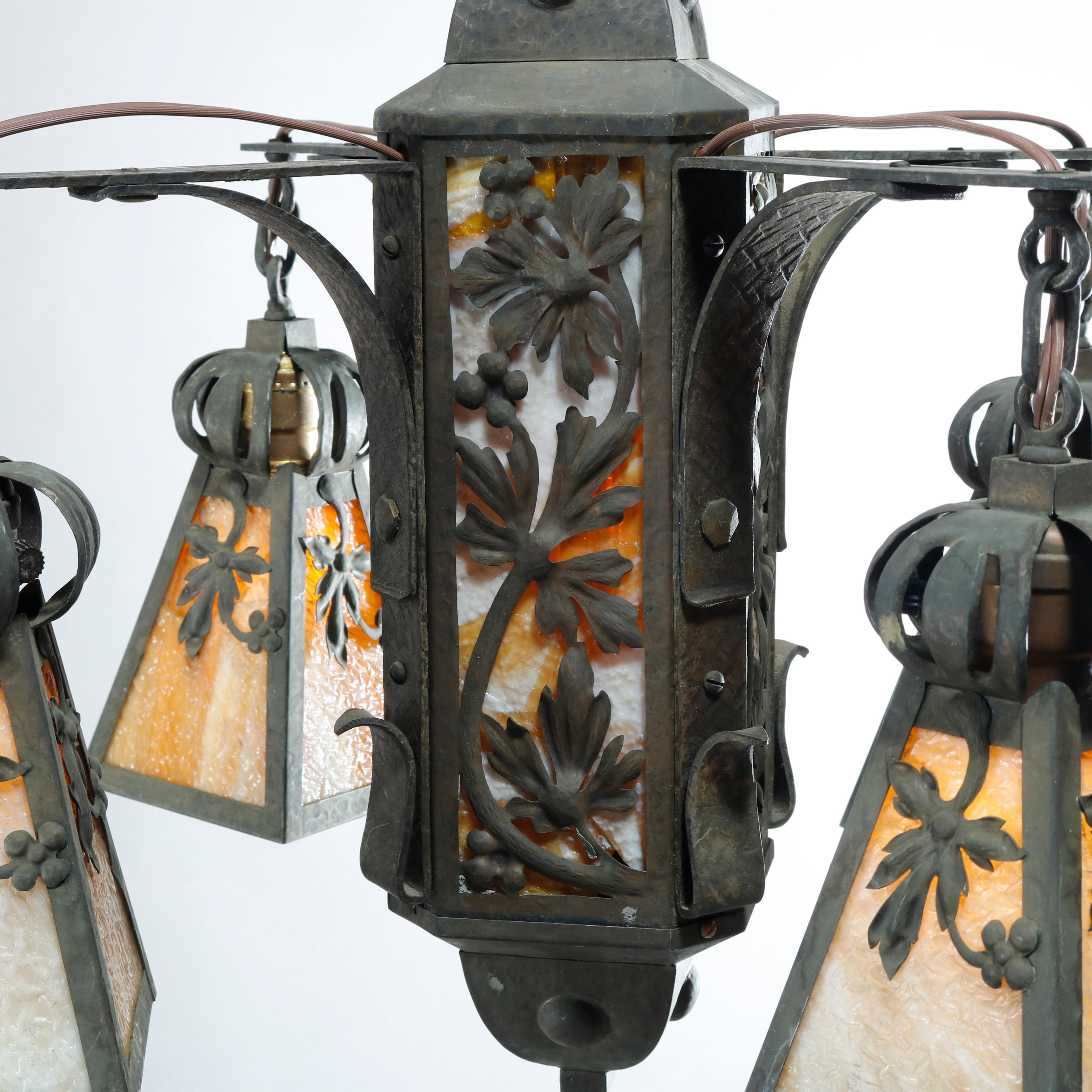 An antique Arts & Crafts ceiling fixture offers wrought iron construction with body having sides with stylized floral elements over slag glass panels and four arms terminating in lantern form drop fixtures, c1910

Measures: 37
