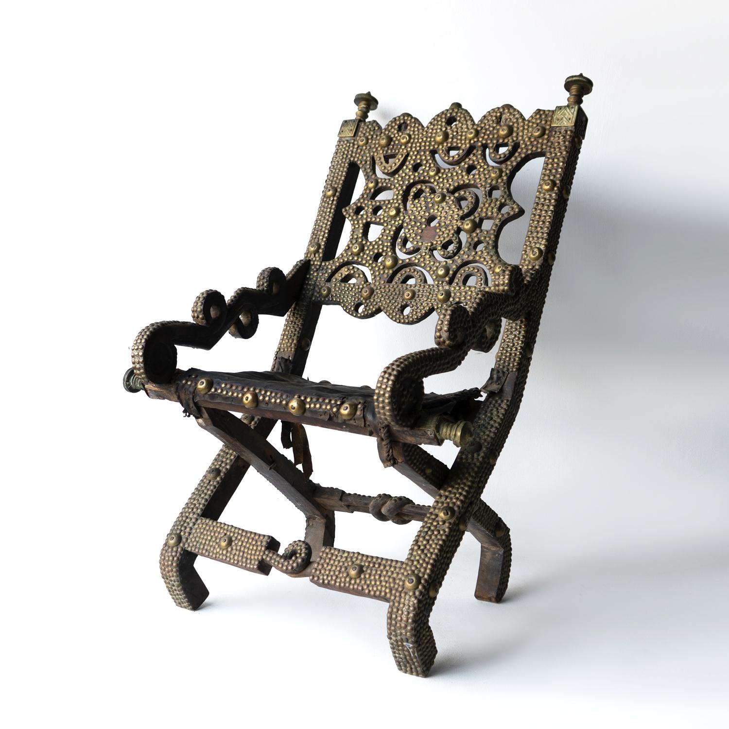ANTIQUE WEST AFRICAN CHAIR

Made from hand-carved hardwood with a leather seat and embellished profusely with brass sheets and studs culminating in decorative brass finials. The carved knot that features on the the front and back rails is known as