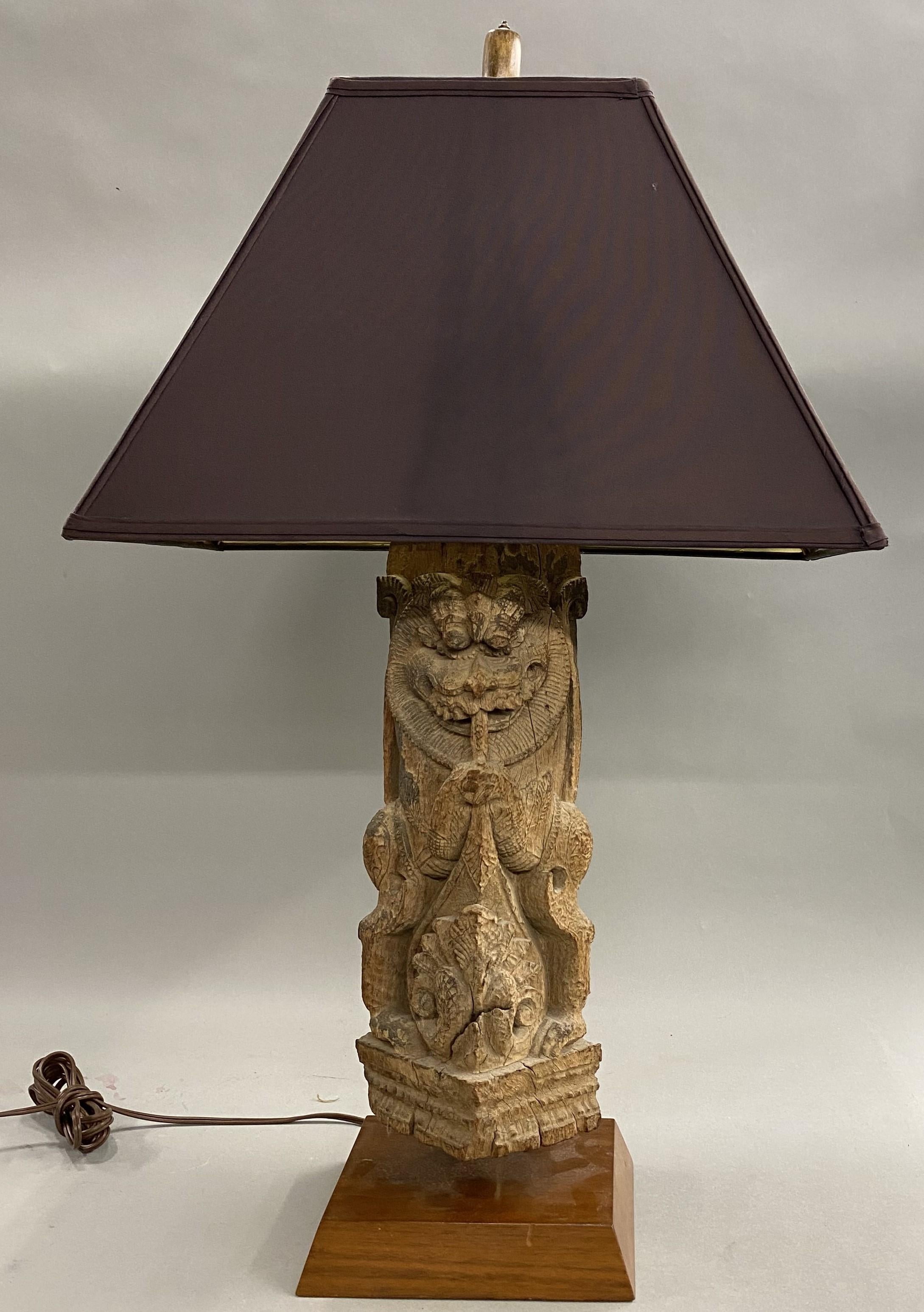 A decorative 19th century Asian carved wooden architectural fragment featuring a horned dragon-like figure, converted to a table lamp with maroon rectangular shade. The lamp is in good working condition, with minimal imperfections and light wear
