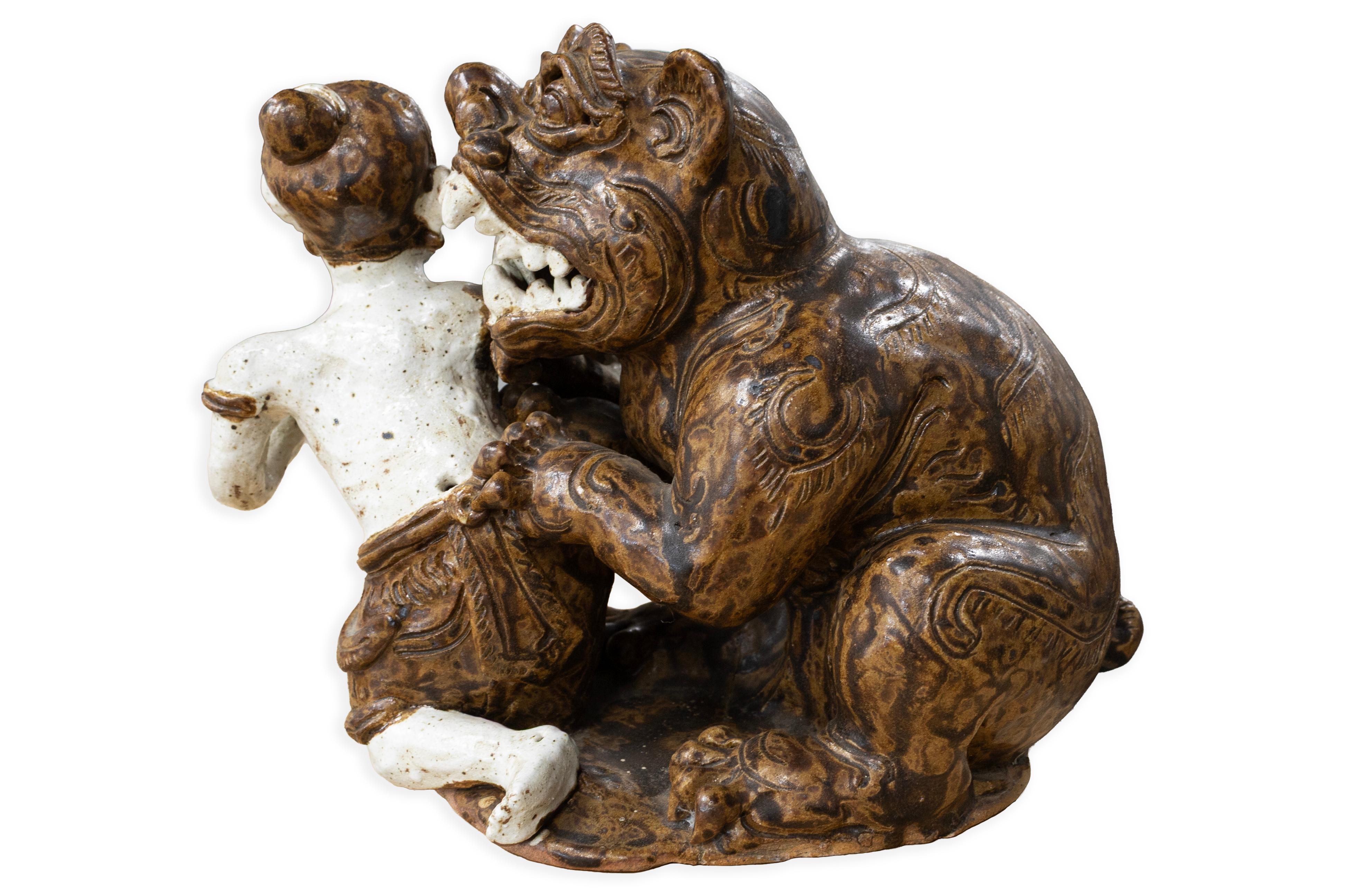 Un'insolita ed espressiva scultura in ceramica asiatica antica che raffigura una figura maschile bloccata in una lotta giocosa con un drago stilizzato o una bestia mitologica. L'opera, realizzata a mano, presenta una figura dal volto sorridente, che