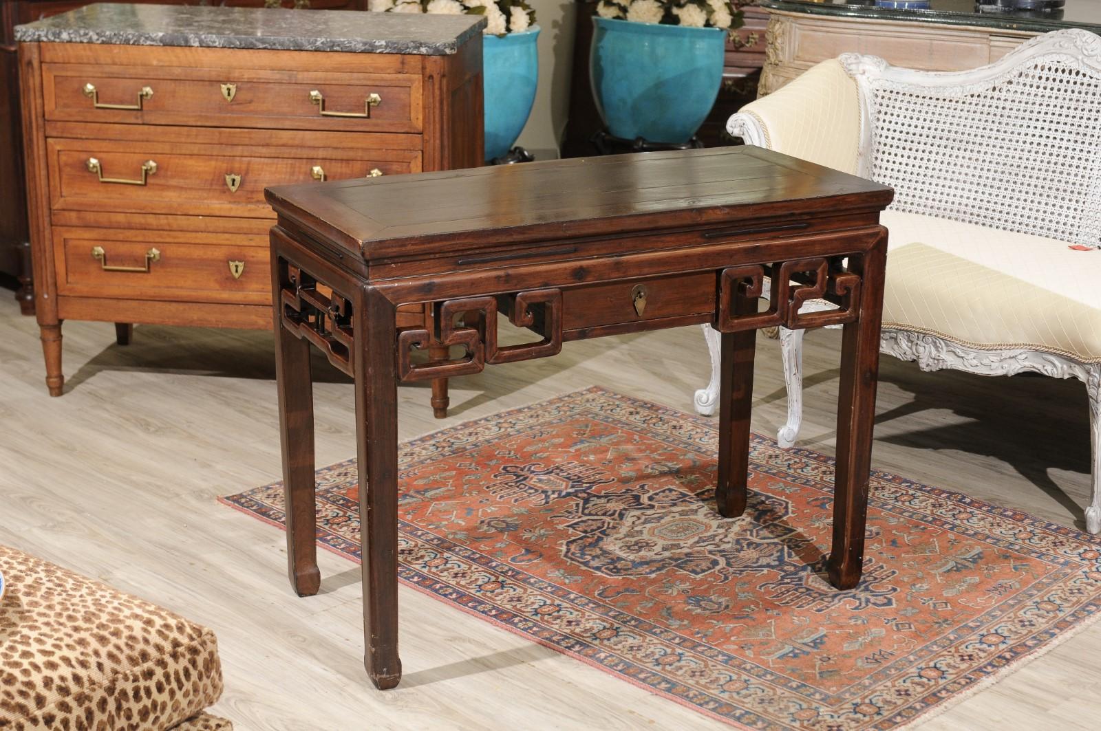 This sturdy wood console may be used as a desk. Simple design would work well in any room of the house. The fretwork on all sides is of the traditional Chinese style. One small drawer is in the center of the table. Supported by four straight legs.