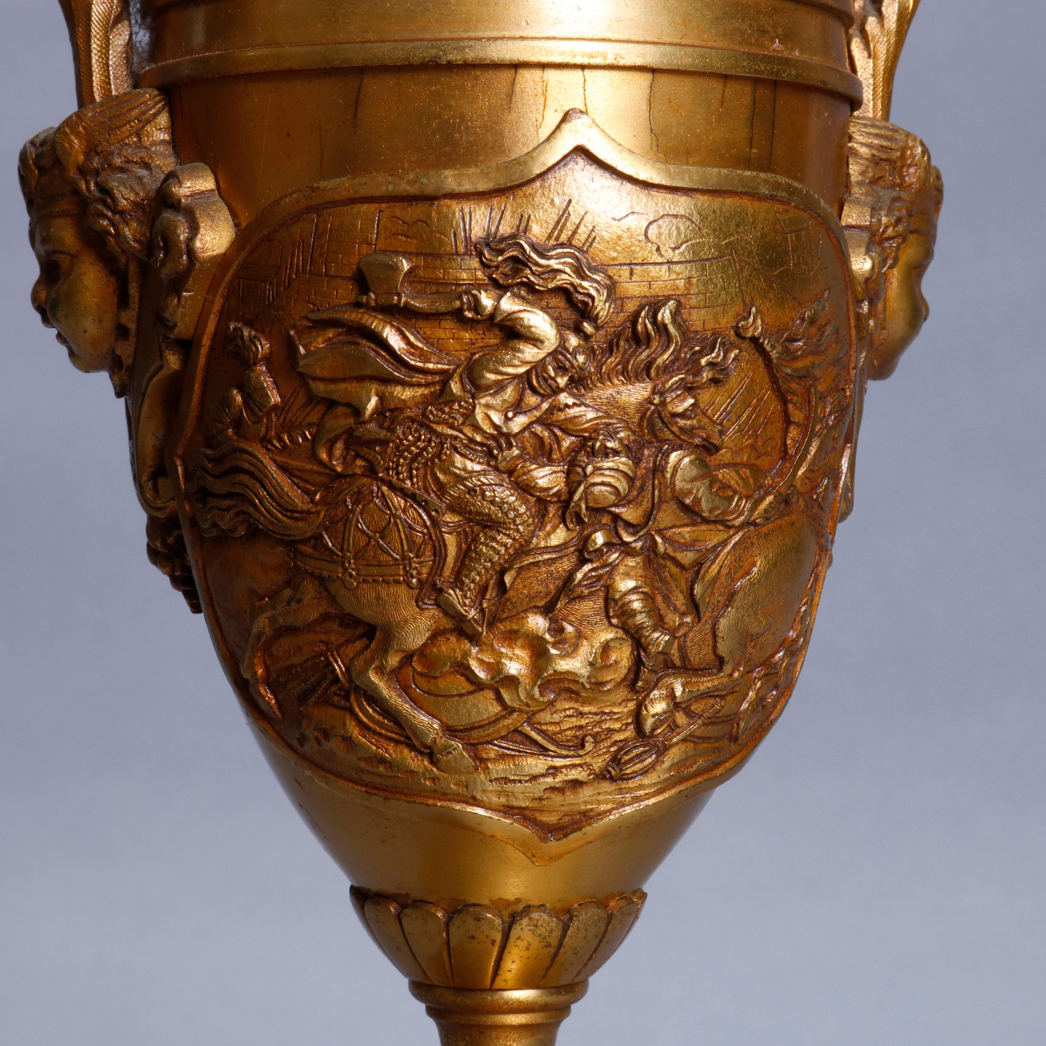 An antique table lamp offers cast and gilt bronze construction in urn form with a reserve depicting an Asian or Moorish battle scene in relief, double Neoclassical cherub mask handles, raised on a stepped and footed plinth having the upside down