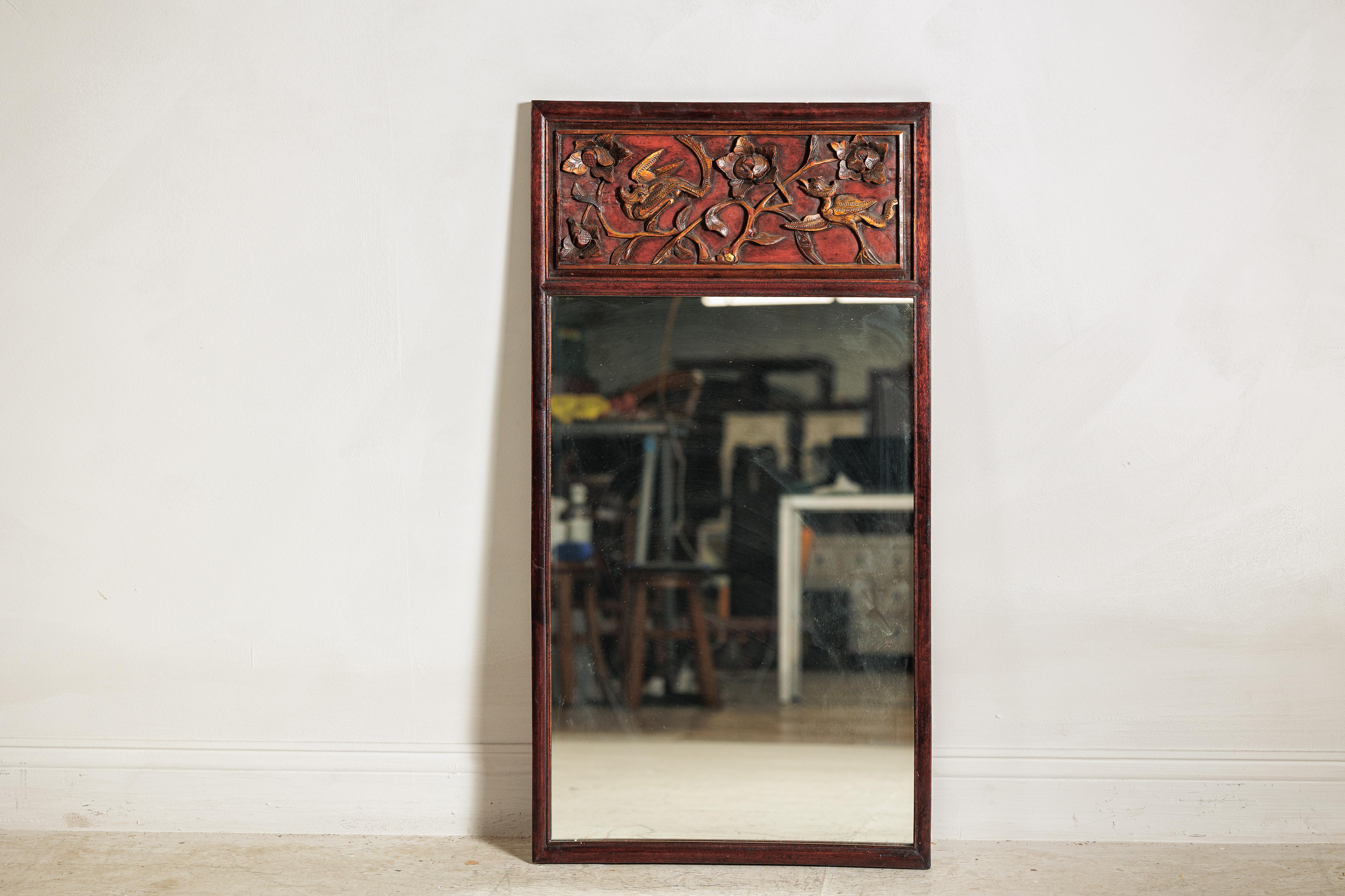 Este antiguo espejo trumeau asiático ofrece una sorprendente mezcla de arte decorativo y forma atemporal. De forma rectangular, la pieza está enmarcada en madera de tonos cálidos y coronada por un panel de cresta tallada. Aquí, los pájaros y las