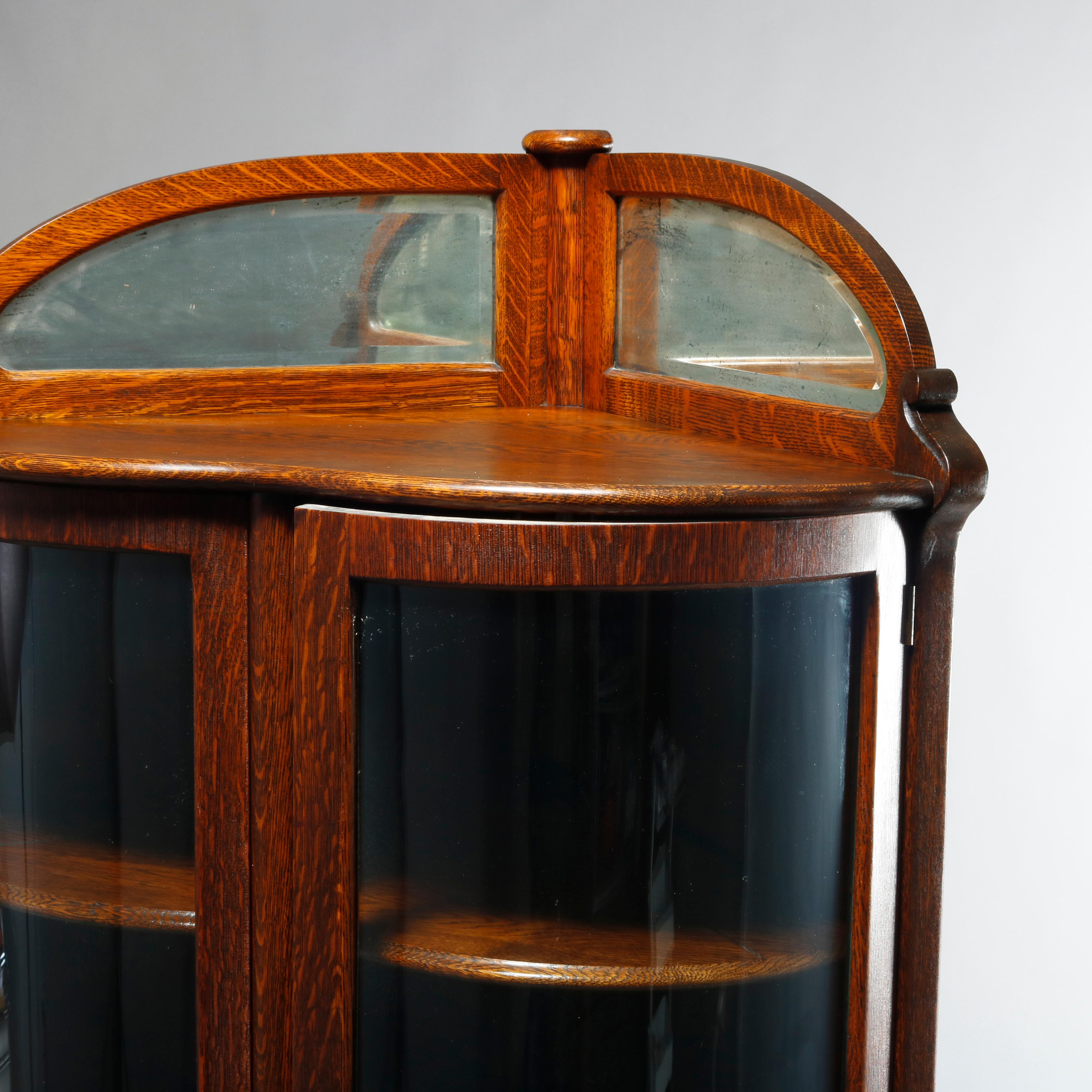 An antique corner display cabinet attributed to RJ Horner offers quarter sawn oak construction in overall heart form with upper mirrored backsplash over shelved case with double curved glass doors raised on cabriole legs terminating in carved paw