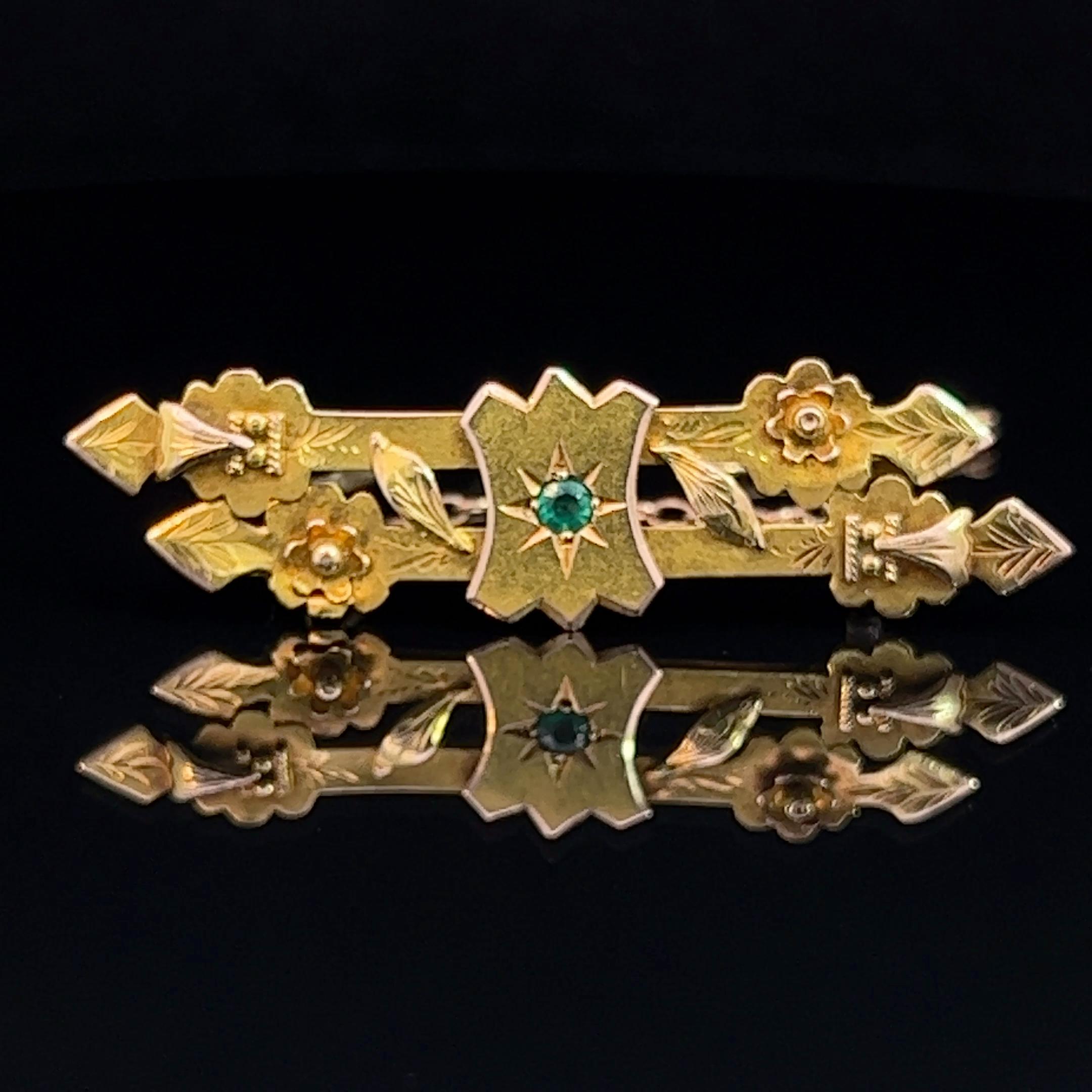 Australian made yellow gold double row, hollow, antique bar brooch. Featuring hand engraving with leaf,  floral, and shield overlay. The shield is set with a small bright green round doublet, possibly a garnet. This brooch has a metal pin and yellow