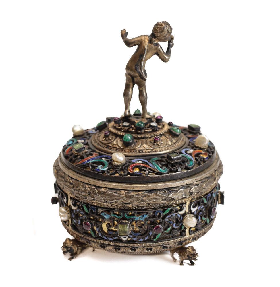 A beautifully ornate Austrian 800 silver, enamel and gem encrusted keepsake box, circa 1900. The stunning box has hand chased leaves to the gilt silver base with a figural cherub to the finial of the lid. Various applied gem adorn the box as well as