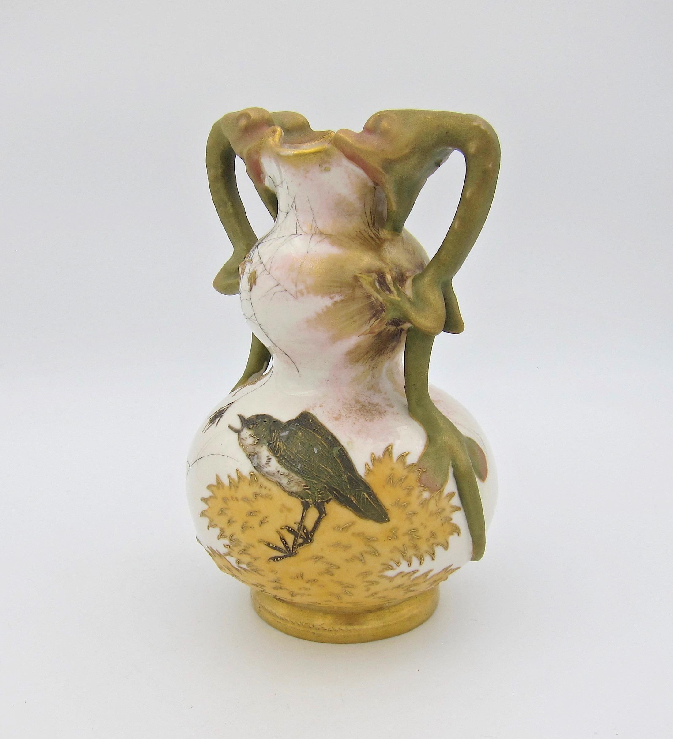 An antique Austrian vase of ivory porcelain by Riessner, Stellmacher & Kessel (RStK) Amphora of Turn-Teplitz, Bohemia (Austria) dating between 1899 and 1900. The vase has two dragon-shaped handles, gilt accents, and hand-painted decor featuring a