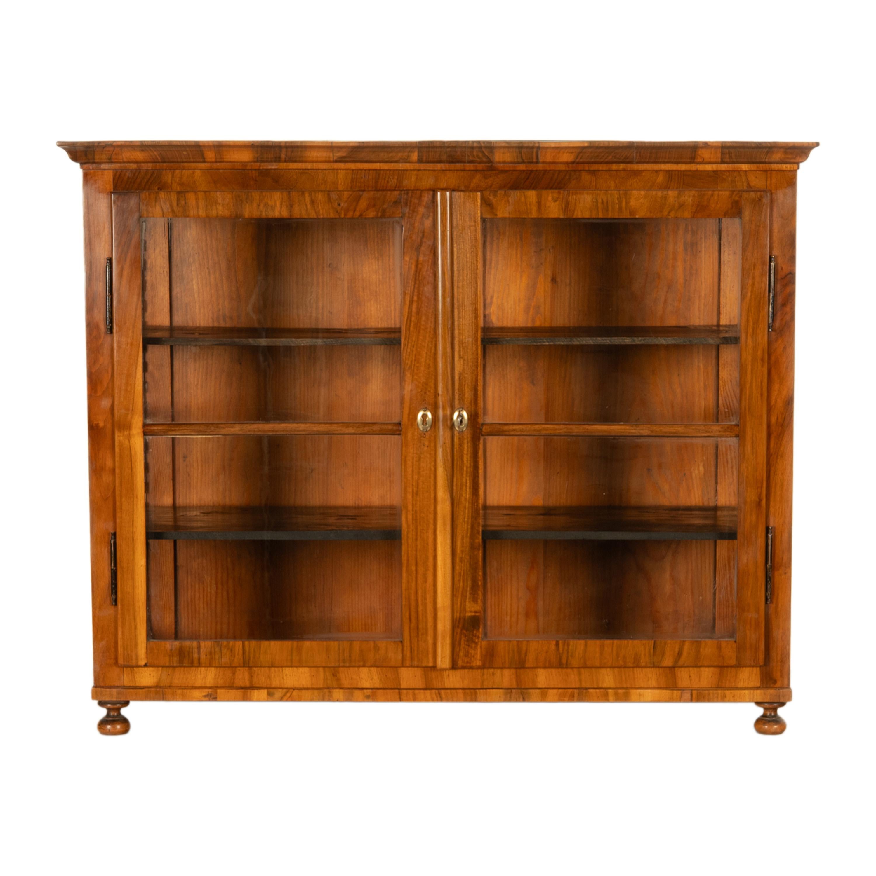 Buena vitrina antigua Biedermeier de nogal con dos puertas, Austria, circa 1820.
Este hermoso armario antiguo tiene una corona en forma de conopio en la parte superior, debajo hay un par de puertas acristaladas con los escudos de latón originales y
