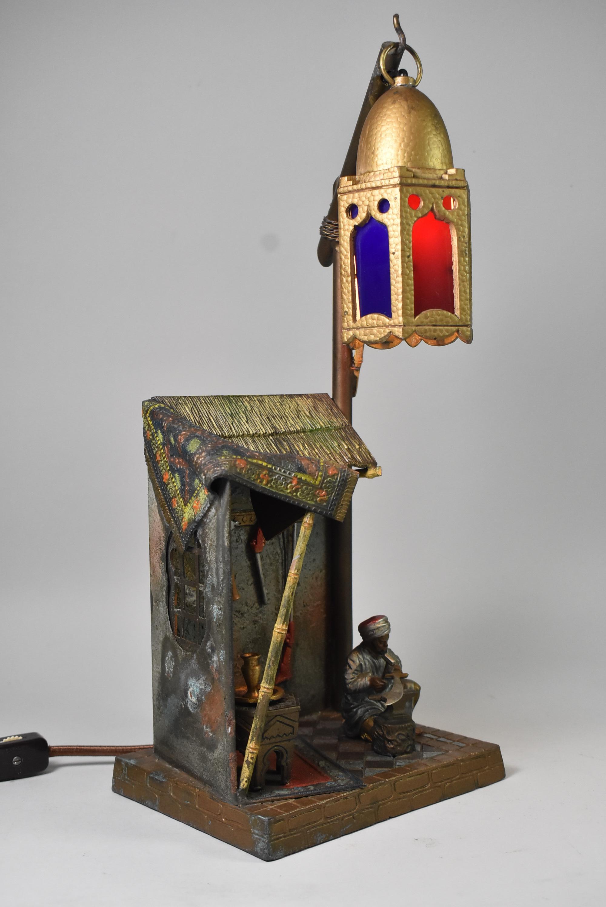 This antique Austrian table lamp is in the style of Bergman. This piece is cold painted and features an Arabian metalsmith. The single socket lantern hangs over a metalsmith's work shop where the craftsman can be seen sharpening a sword. 14 3/4