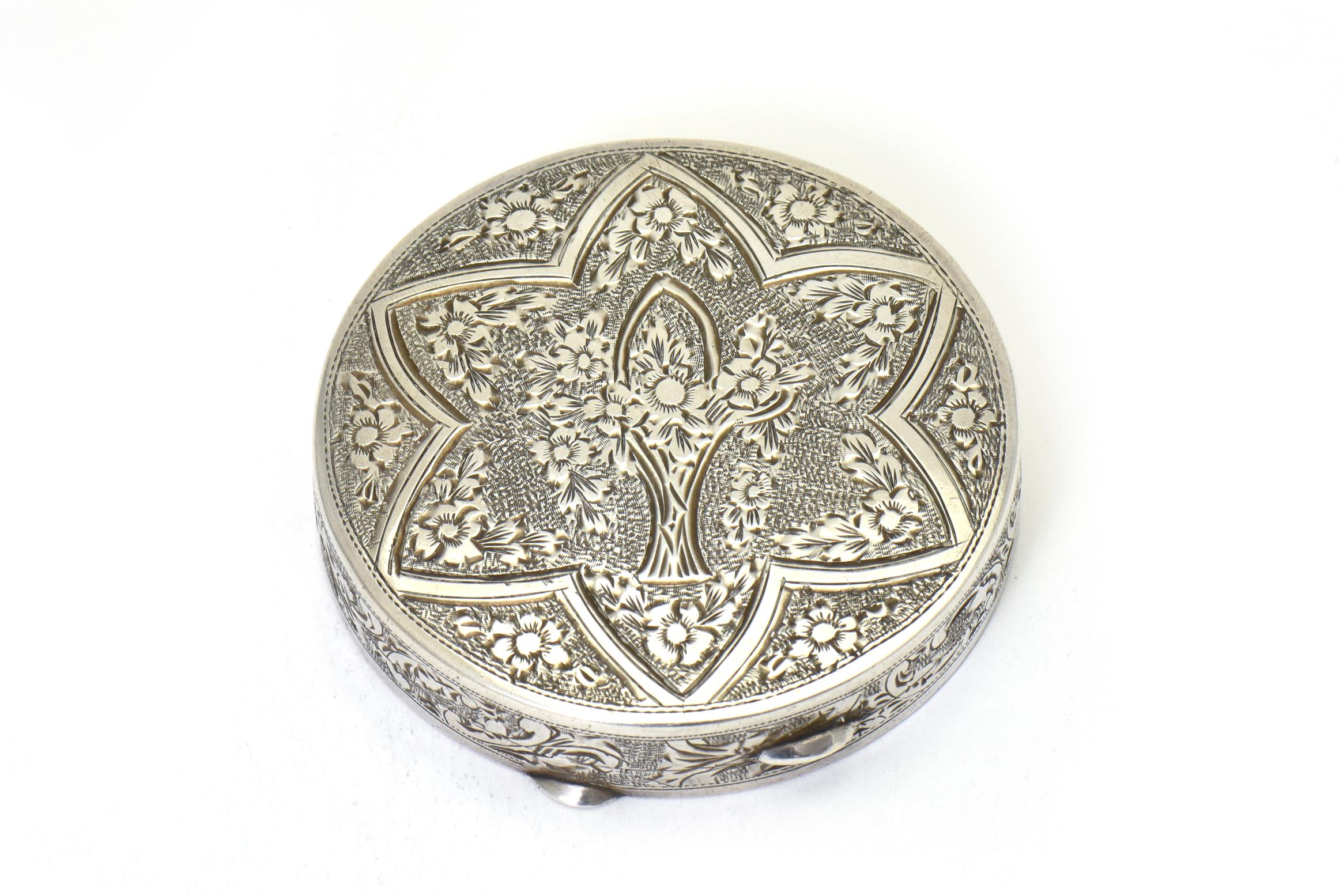 Beautifully made hinged silver compact featuring a floral design on the top section with a flower basket in the middle of a floral wreath and star. There are more flowers on the outer edge. Inside is a beveled glass mirror with a twist rope border,