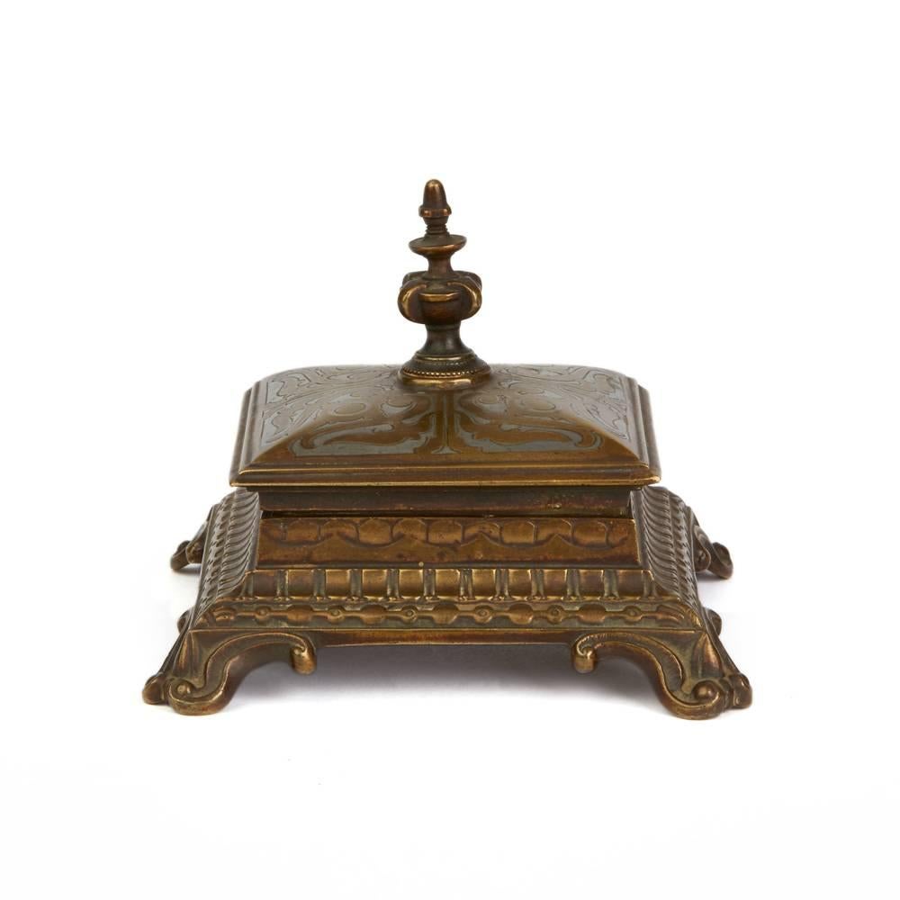 A fine antique Austrian or possibly German inlaid bronze desk stamp holder/lick standing raised on four scroll work feet with a hinged cover with central raised knop, the cover inlaid in silver coloured metal with a scroll work design. The cover