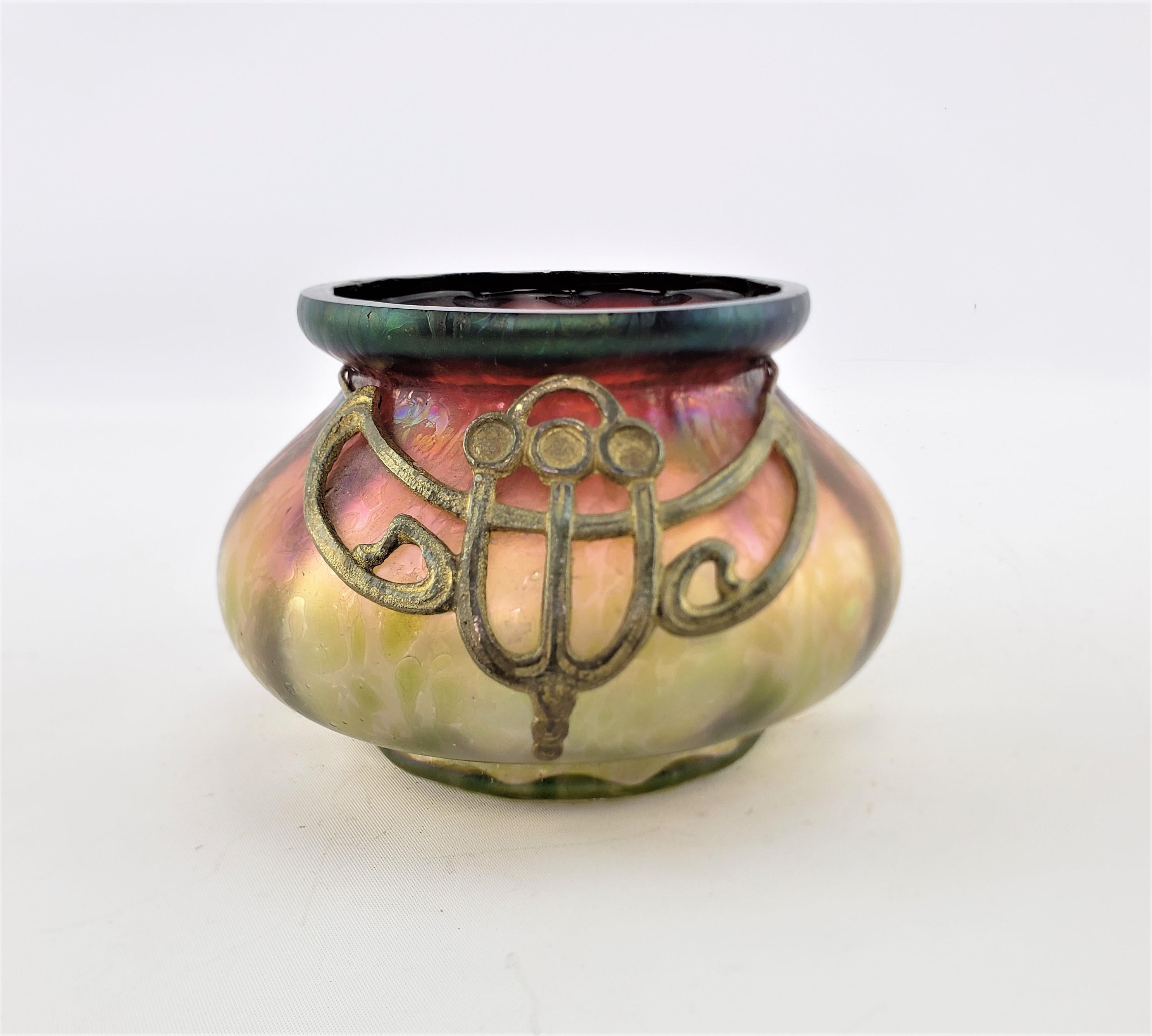 This antique art glass vase is unsigned, but presumed to have originated from Austria and dates to approximately 1900 and done in the period Art Nouveau style. The vase is done in multi colors with strong iridescence and has a hand hammered cast