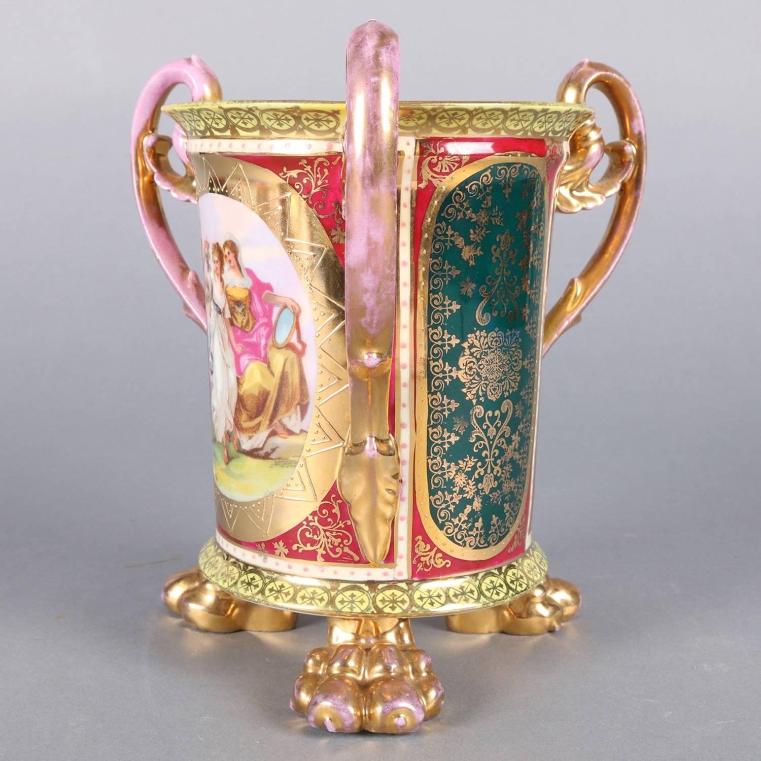 Antique Austrian Royal Vienna porcelain loving wedding cup features hand painted panels with front having reserve depicting bride with her maids and scrolled gilt highlight throughout, three scroll form handles and seated on three gilt lion paw