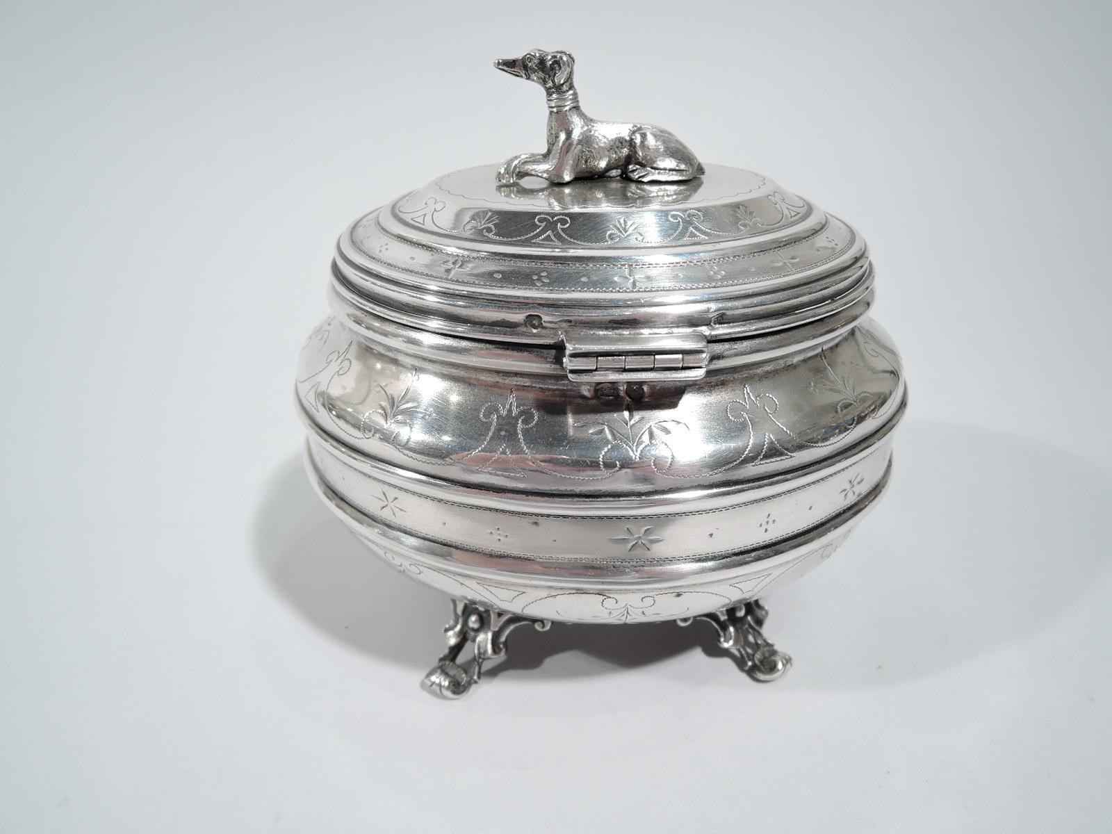 Austrian 800 silver box, circa 1910. Oval with double girdle and hinged and raised cover. Four fancy scroll and shell supports. Pointille scrolled bands and engraved stylized flowers. Cover top has cast canine finial in form of recumbent greyhound.