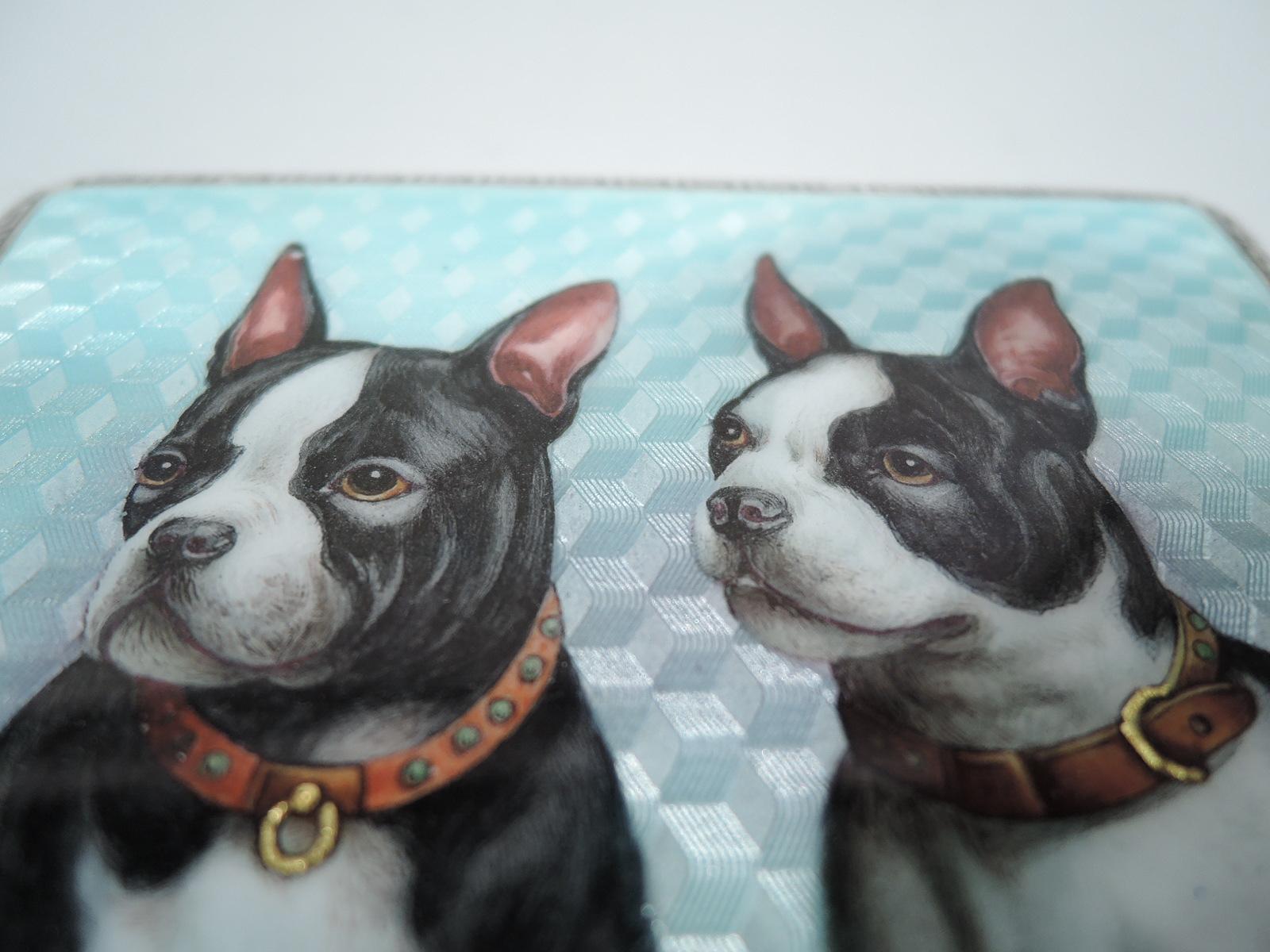 Austrian silver and enamel cigarette case, ca 1910. Rectangular and hinged. On cover is enameled doggy double portrait: 2 Boston terriers with erect ears and steadfast gaze. The studded leather collars suggest they’re taken. Companionable canines on
