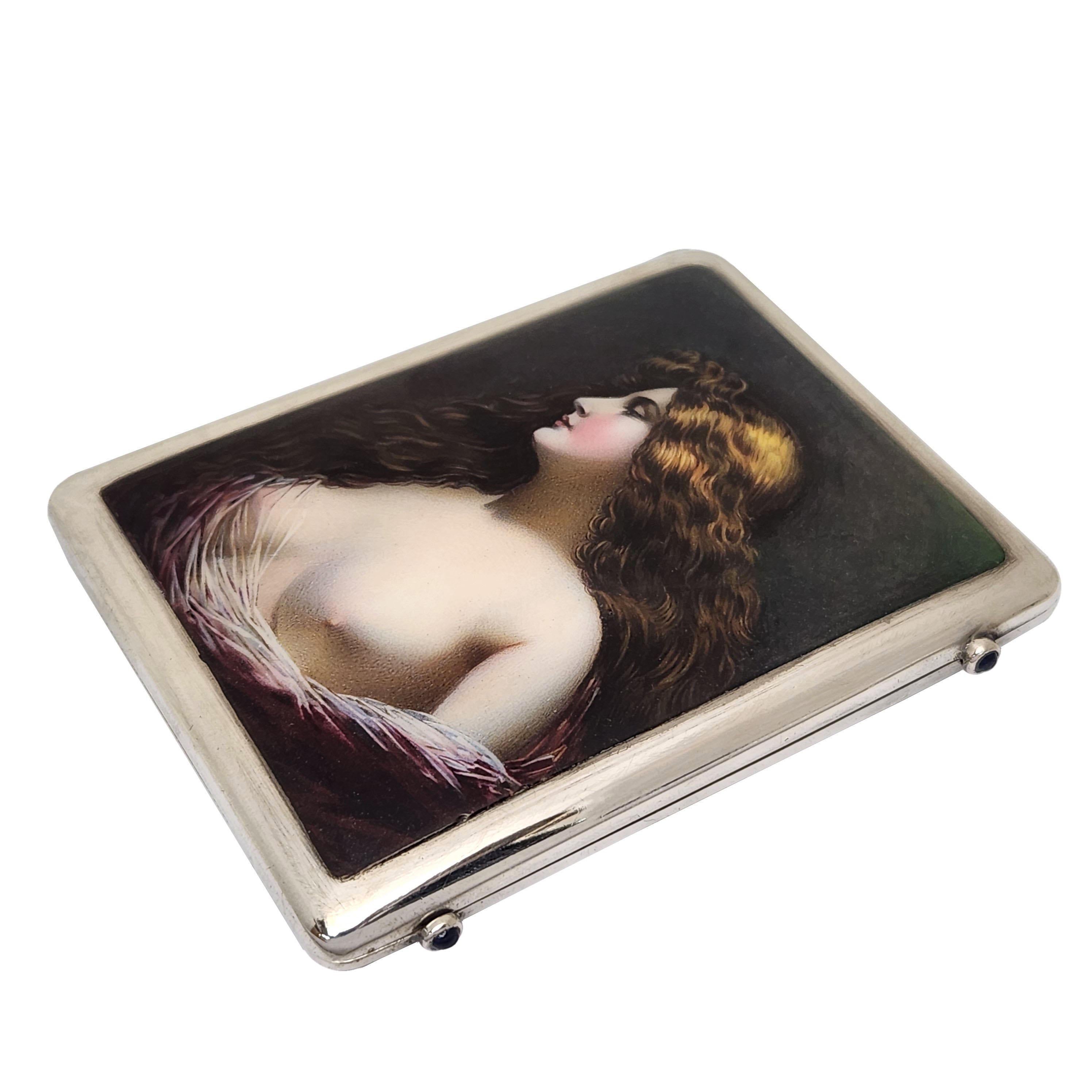 A beautiful Silver Cigarette Case decorated with a beautiful Enamel Image on the front of the case. The Image shows a woman with rich golden brow hair covered in part with a diaphanous wrap and with her breasts exposed. The Case has a pair of