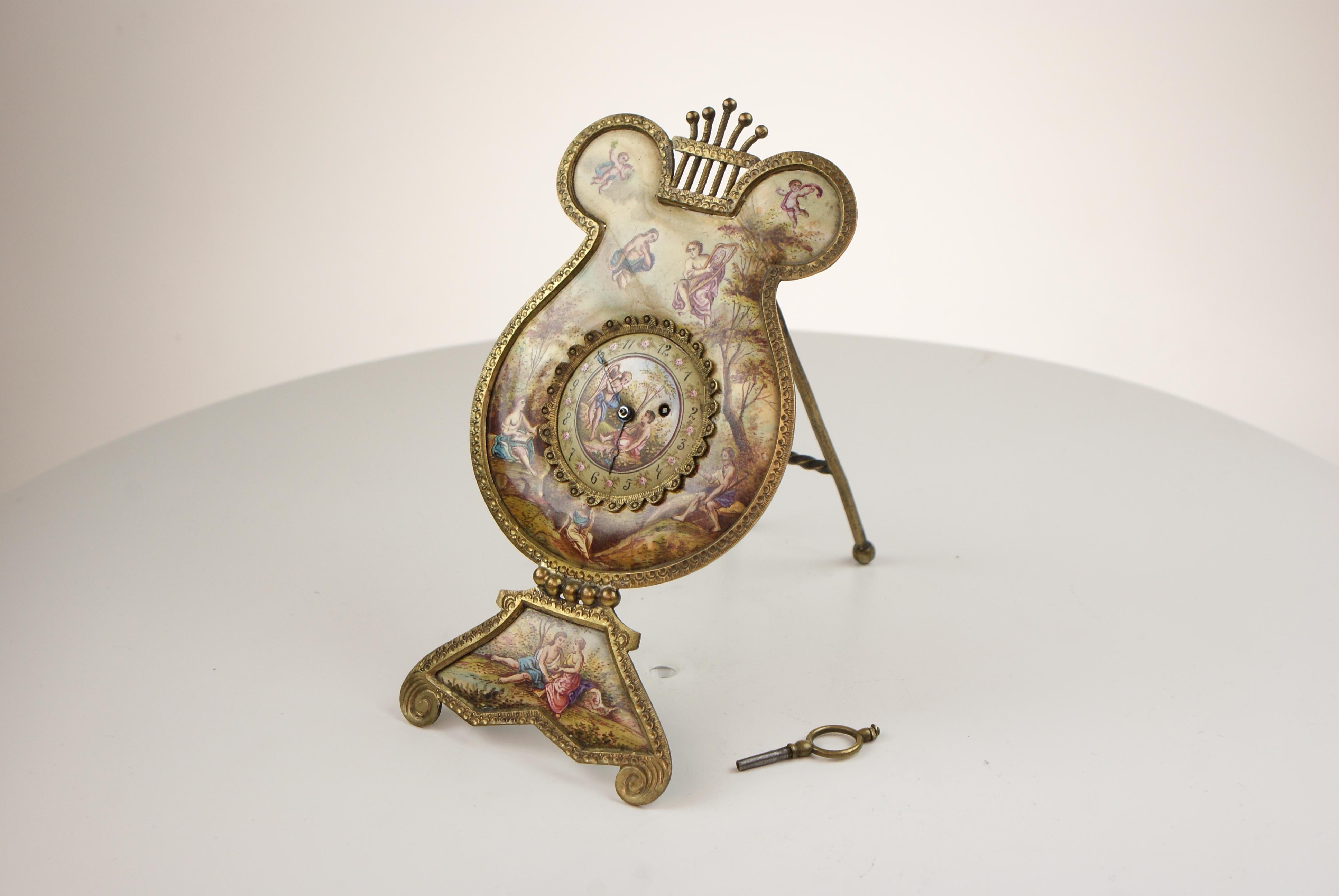 Antique Austrian Viennese hand painted enamel gilt metal lyre clock,

In the form of an artist palette on an easel painted with scenes of cherubs. The clock face similarly painted the numbered dial also painted with intimated roses. The back