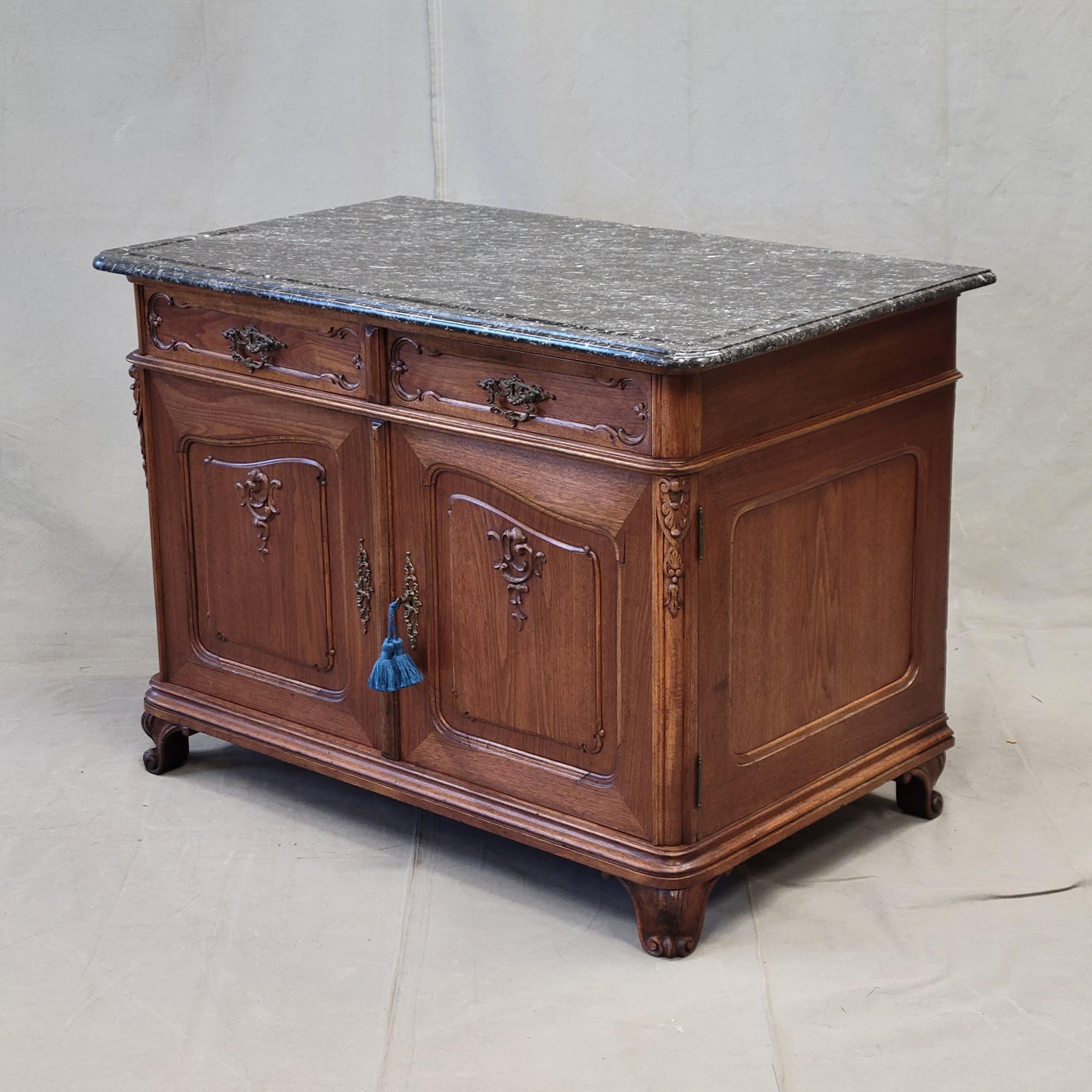 An elegant early 1900s Austrian (in the French style) walnut buffet or washstand with an antique black marble top. Beautifully crafted of pine and oak in the interior with thick walnut veneer on the exterior. The applied carving and brass hardware