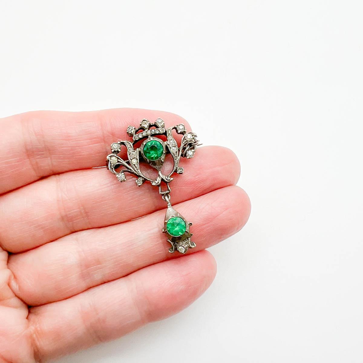 Una deliziosa spilla antica austro-ungarica. Un design a corona in argento massiccio con pietre in pasta di vetro chiaro e smeraldo. Il retro con motivi intricati o cesellati è un segno distintivo dell'artigianato austro-ungarico. La scala in