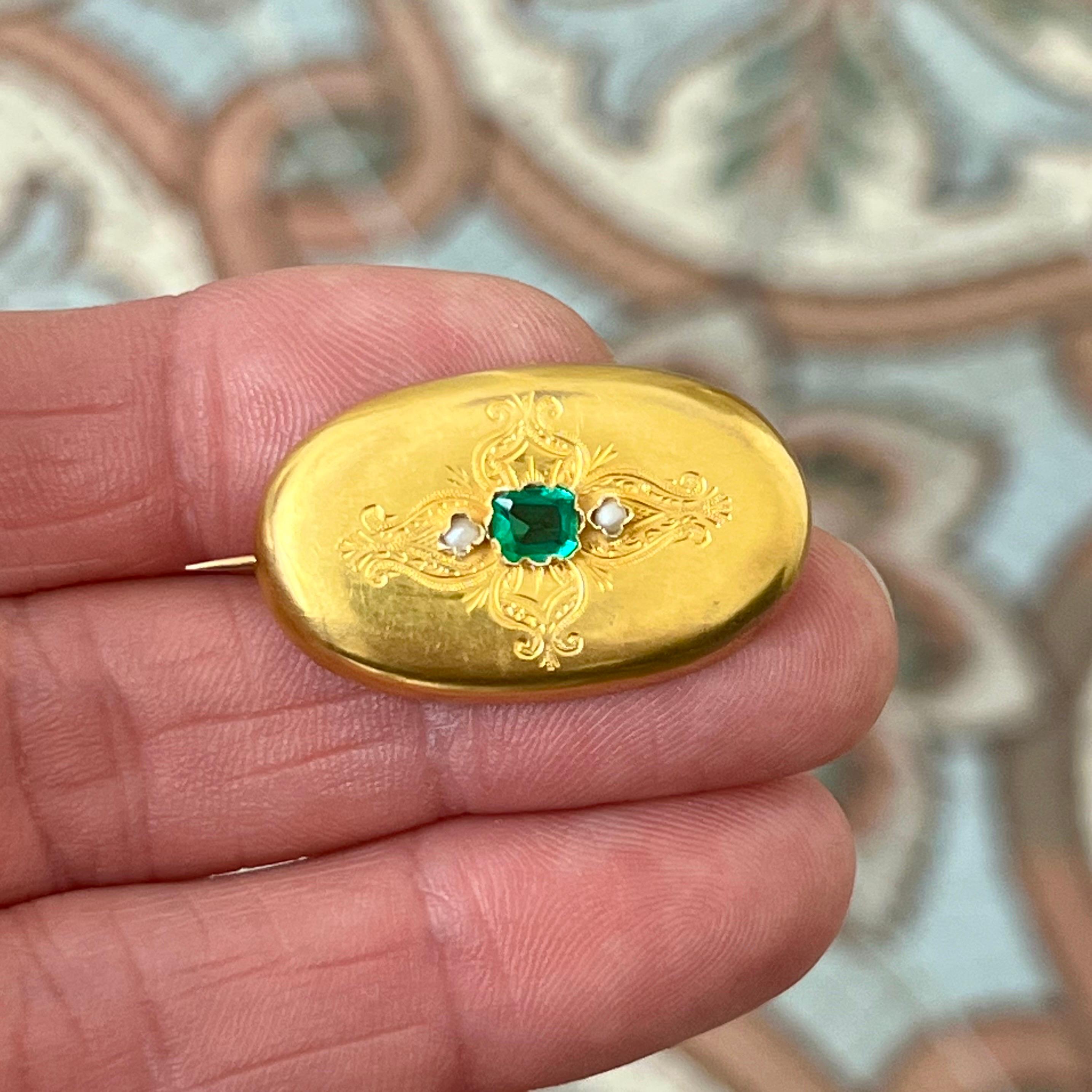 Cette élégante broche ovale est un bel exemple de l'artisanat austro-hongrois du milieu du XIXe siècle. Réalisée en or jaune 14 carats, cette broche présente une surface finement gravée, ornée en son centre d'une pierre en pâte verte de taille