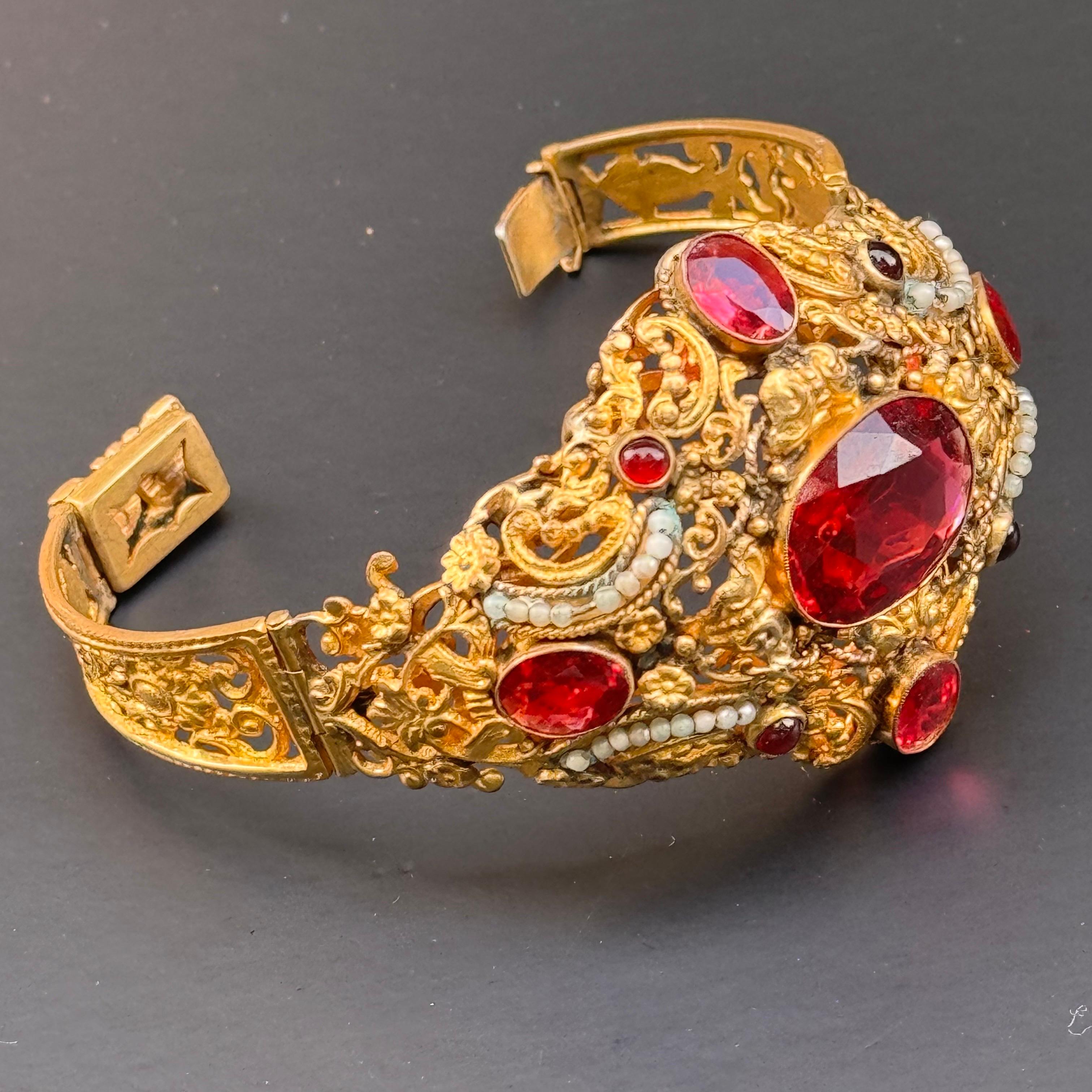 This exquisite bracelet, dating from the first half of the 20th century, showcases the remarkable craftsmanship of Austro-Hungarian jewelry. The wide band features vibrant, faceted garnet glass cabochons set in a luxurious gold gilt, accented by