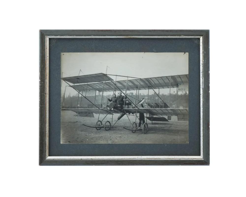 An antique black and white photograph depicting a side view of the Bristol military type biplane with a couple seated on the biplane. The balancing planes and method of supporting the extensions of the top plane are very prominent in this