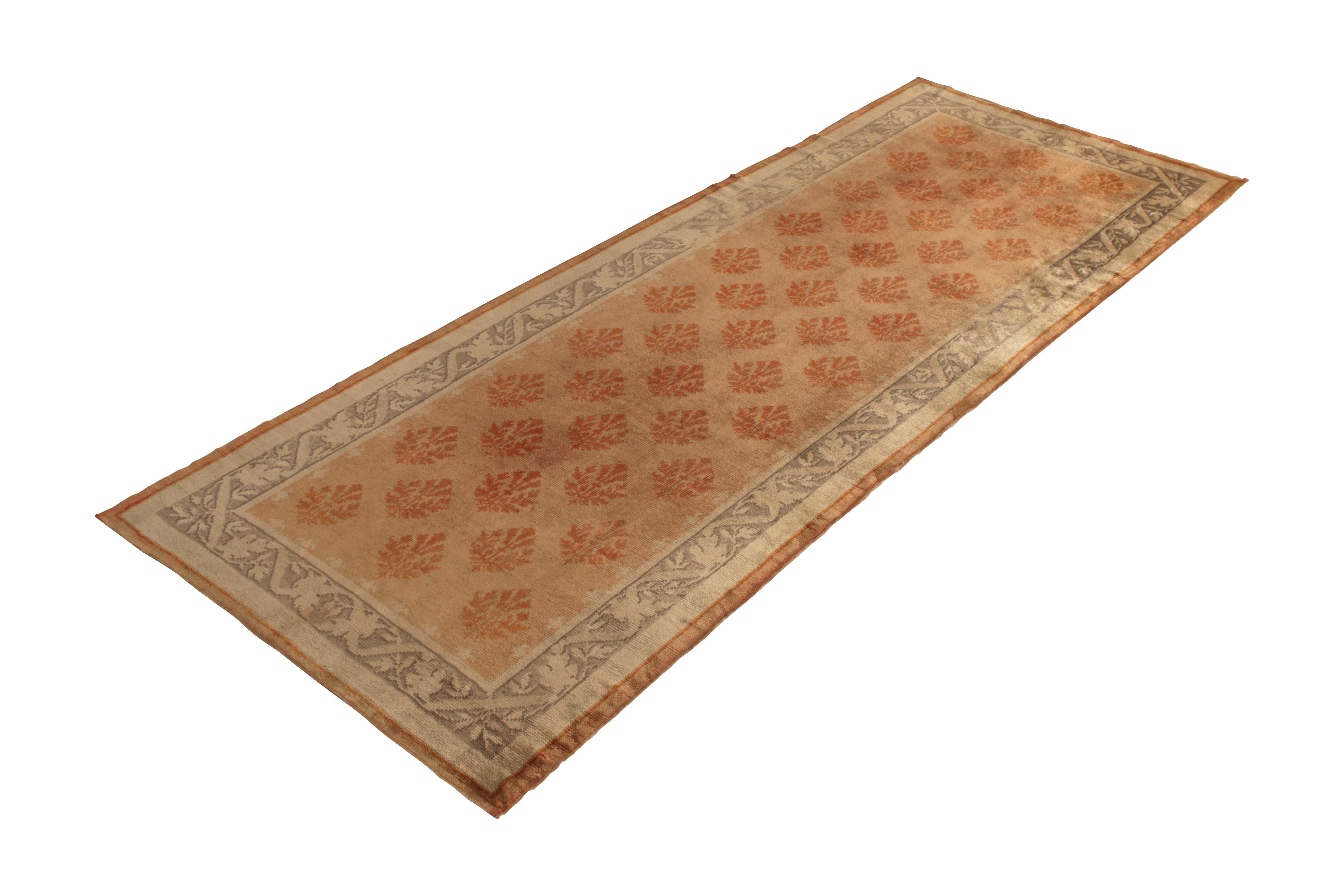 Hand knotted in wool originating from England circa 1910-1920, this Axminster antique rug enjoys rare gallery size dimensions and an atypical play of peach orange and beige-brown hues. This particular traditional rug idealizes the subtle variations