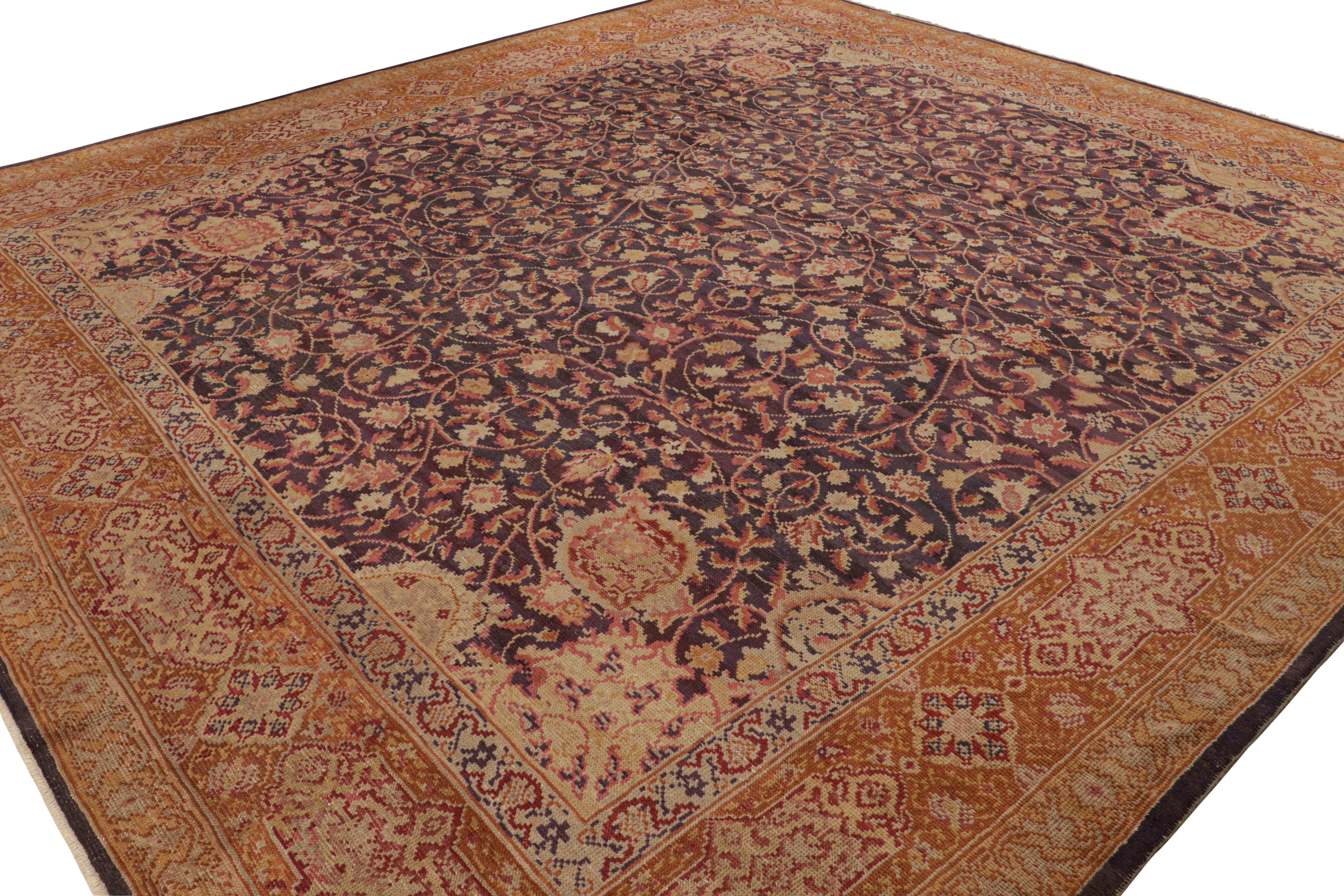 Originaria de Irlanda, hacia 1910-1920, esta alfombra antigua de Axminster mide 12'8 x 13'8 y está hecha a mano con lana anudada a mano. El beige y el naranja son los colores dominantes, con un notable fondo de campo azul que complementa los tonos