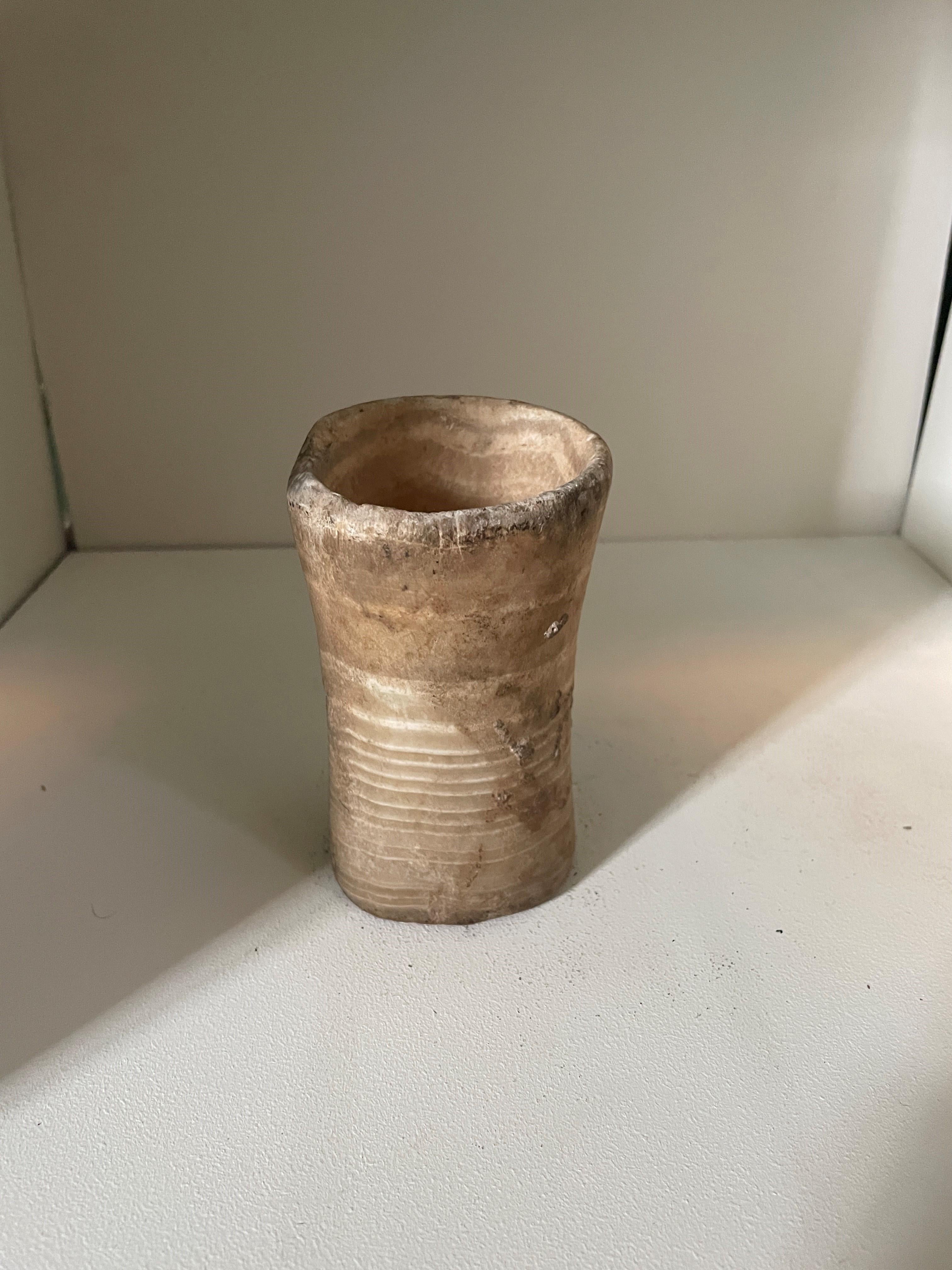 Bactrian Alabaster offering vessel, second millennium BC, A small veined alabaster vessel with asymmetric waisted cylindrical form. The interior half way down in a U boul. Composite residue in and outside the vessel. Beautiful veining with typical