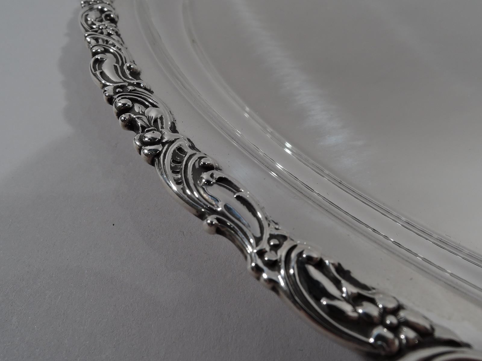 Turn-of-the-century sterling silver serving tray. Retailed by Bailey, Banks & Biddle in Philadelphia. Round; rim everted and applied with scrolls and flowers. Fully marked including maker’s (Fuchs) and retailer’s stamps, and no. 231. Weight: 22.5