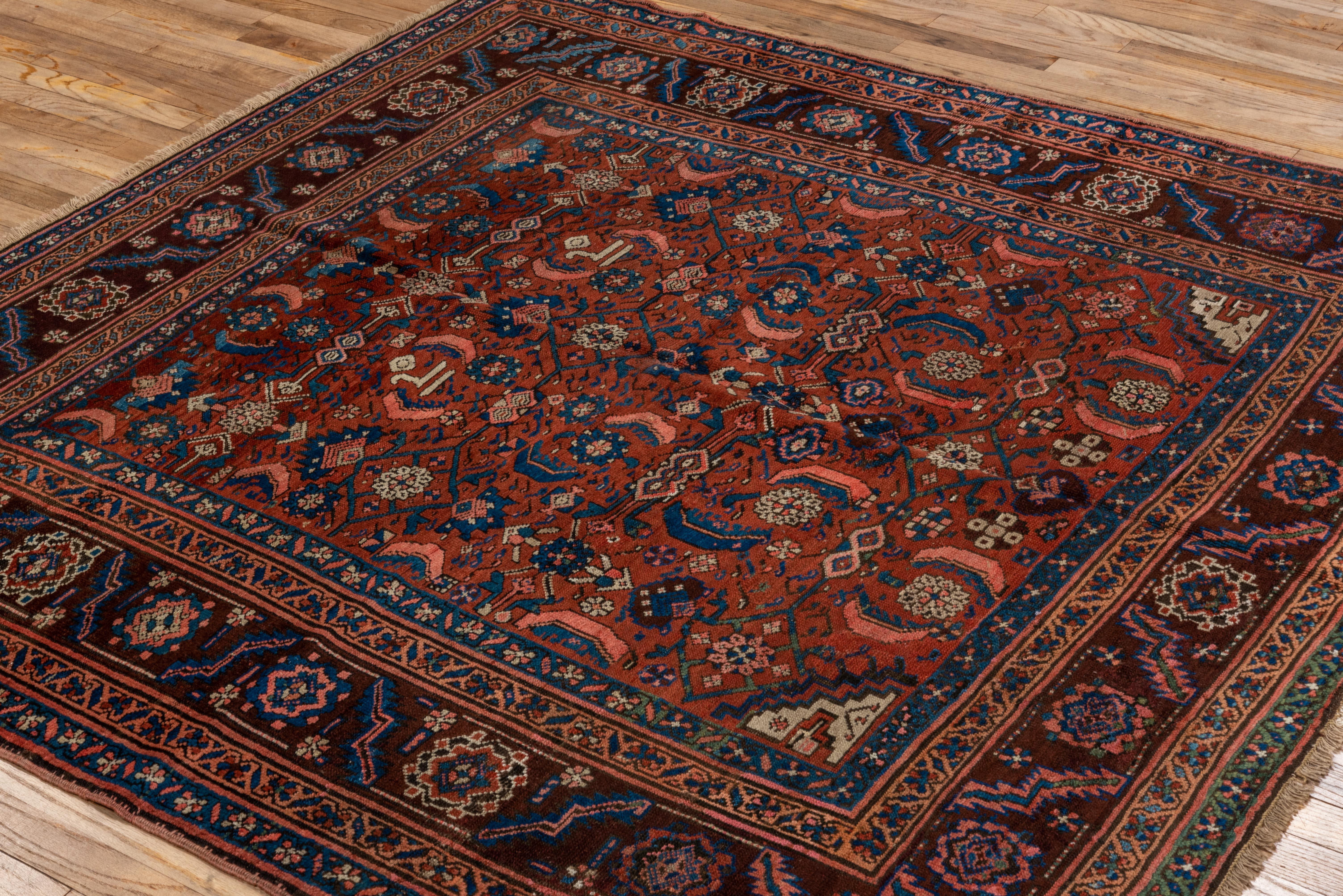 This antique Bakhshayesh rug is a striking square-format piece characterized by a bold coral red field richly adorned with stylized palmettes, rosettes, and serrated leaf forms. Hints of indigo, ivory, sky blue, and brick create a dynamic visual