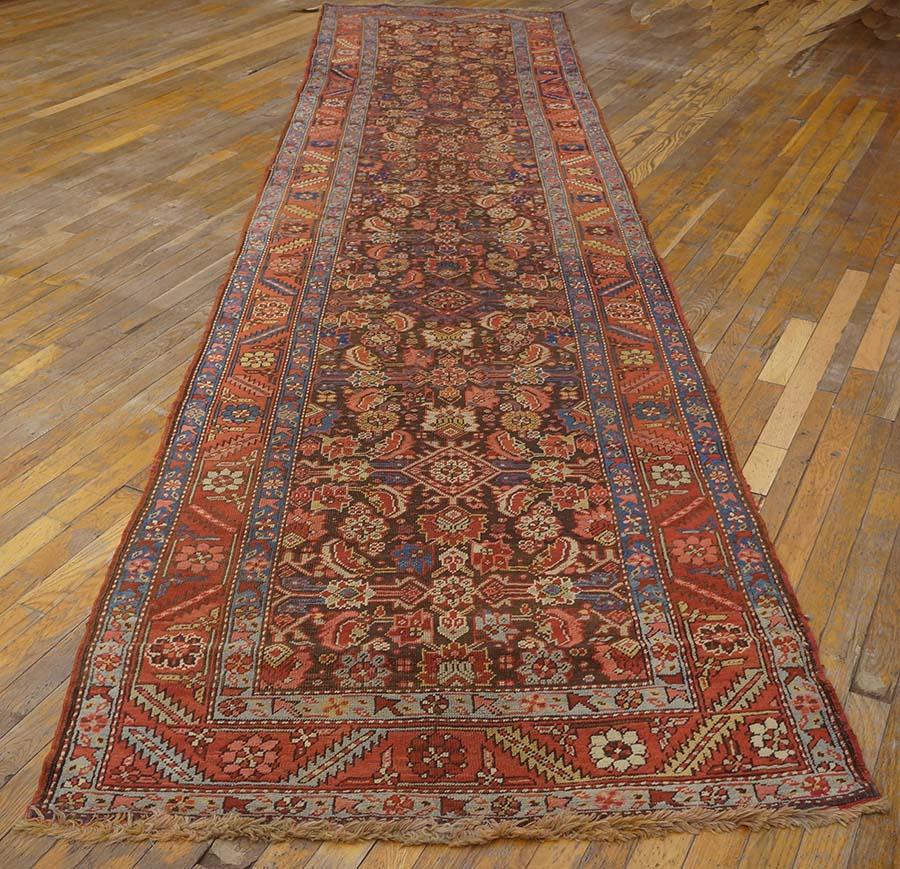Das etwas korrodierte, dunkelbraune Feld dieses breiten Kenare (Läufer) im persischen Format zeigt ein Herati-All-Over-Muster in Flachrelief, das in Creme, Sand, Rot und Marinefarben ausgeführt ist. Das Muster hat eine starke, lange Zentralität mit
