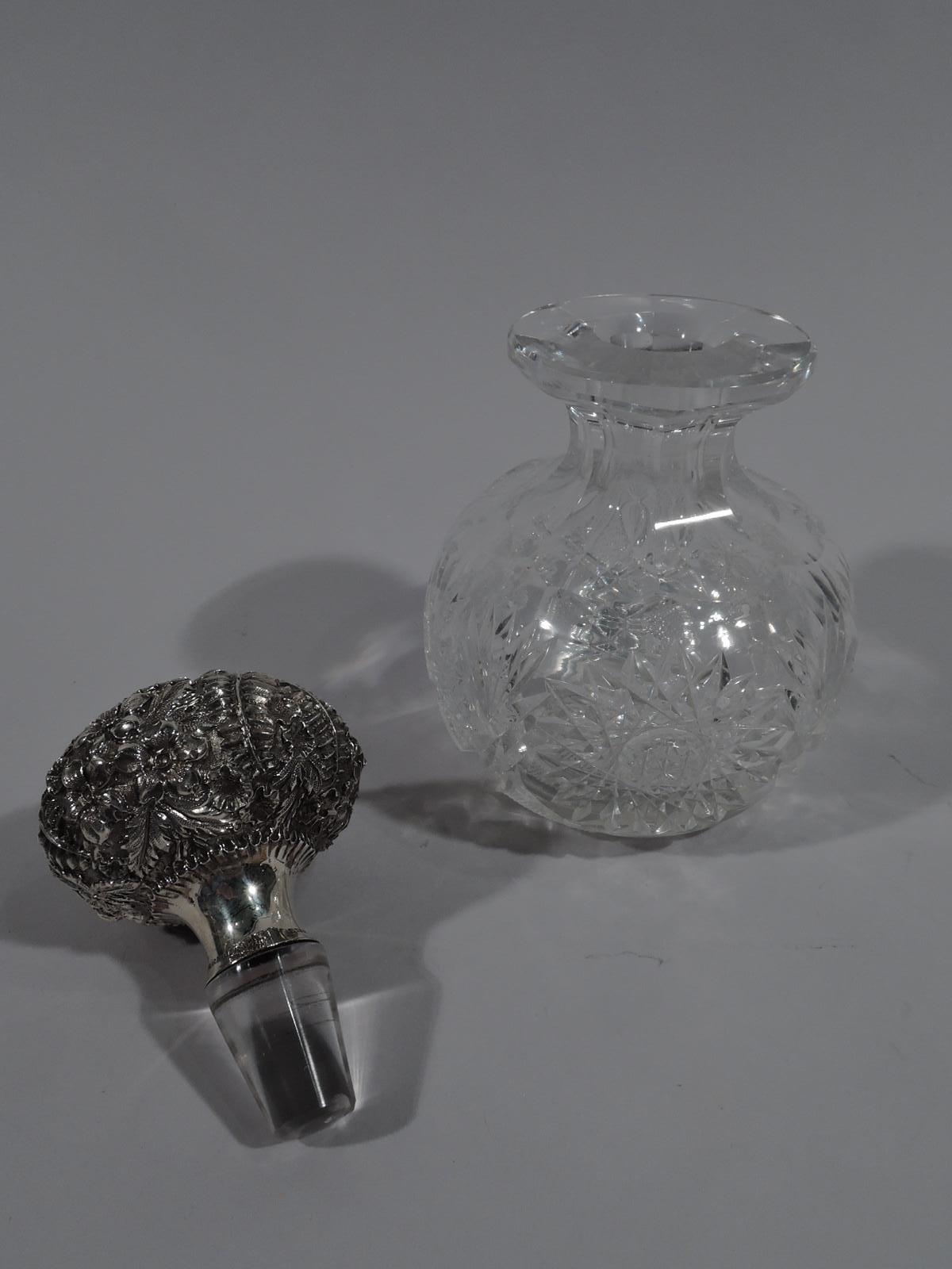 Turn-of-the-century cut-glass perfume bottle with sterling silver stopper. Globular with short and faceted neck and shoulder, and everted rim. Star, fern, and diaper ornament. Globular stopper with dense repousse-style flowers and ferns on stippled