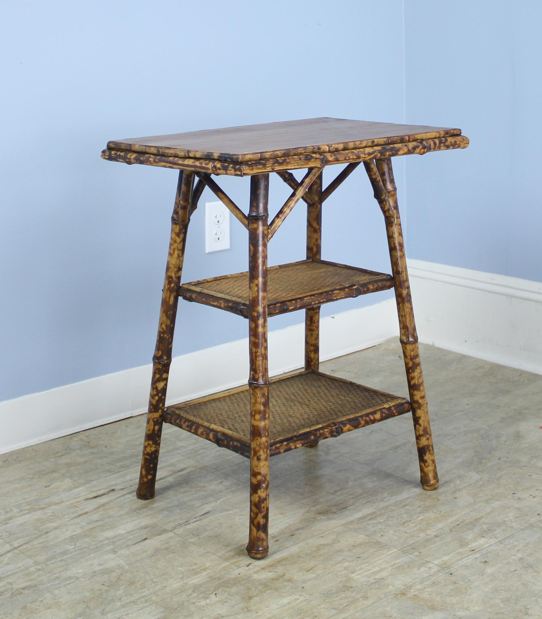 An antique English bamboo side table, with flared legs and with three shelves. The top is wood, with good color and patina, the bottom shelves made of tightly woven rush. The bamboo, vividly painted, is in good sturdy condition. Charming as an end