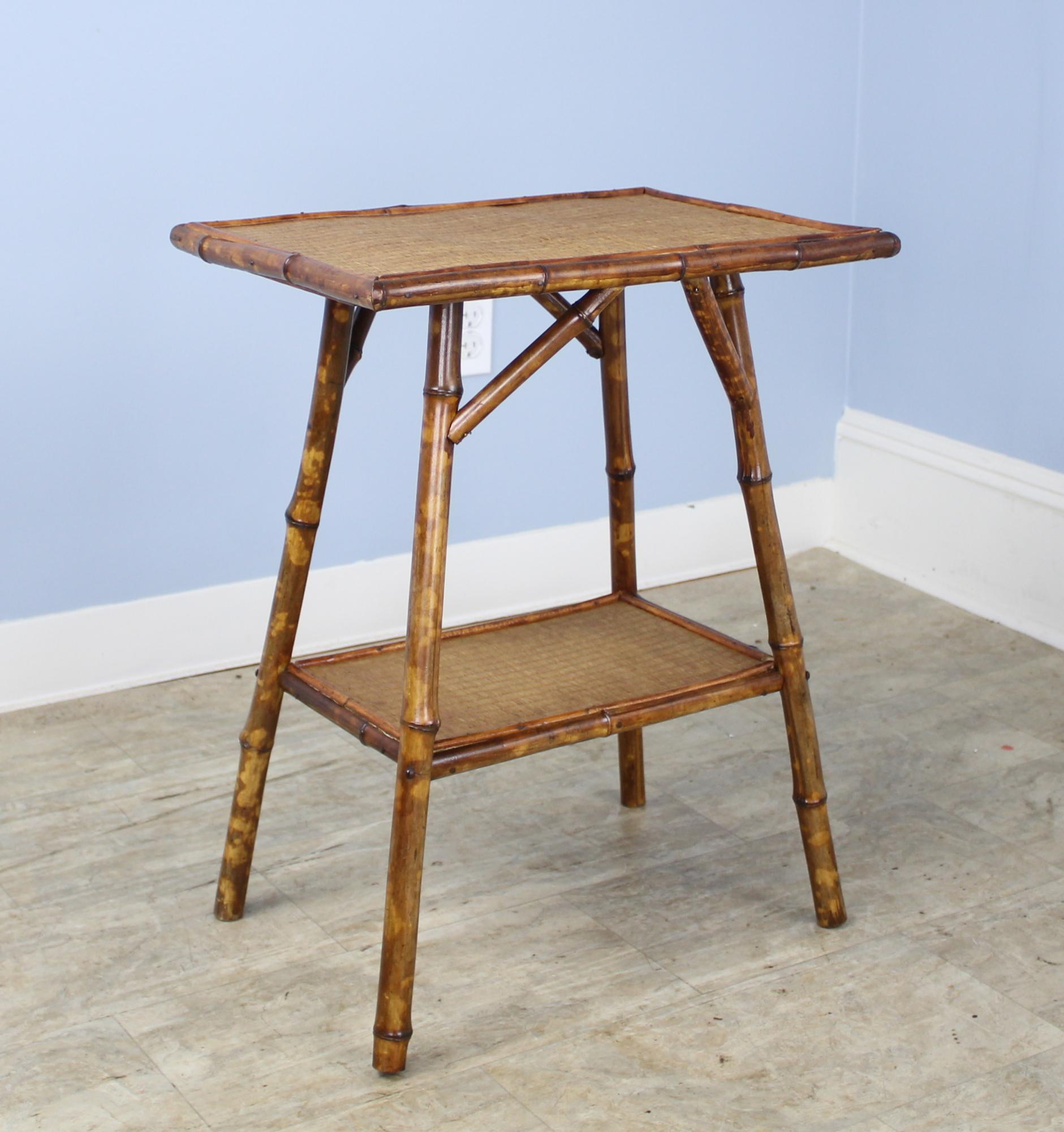 An antique English bamboo side table, with flared legs and with two shelves. Both shelves are made of tightly woven rattan that is in very good condition. The bamboo, vividly painted, is in good sturdy condition. Charming as an end or lamp table.