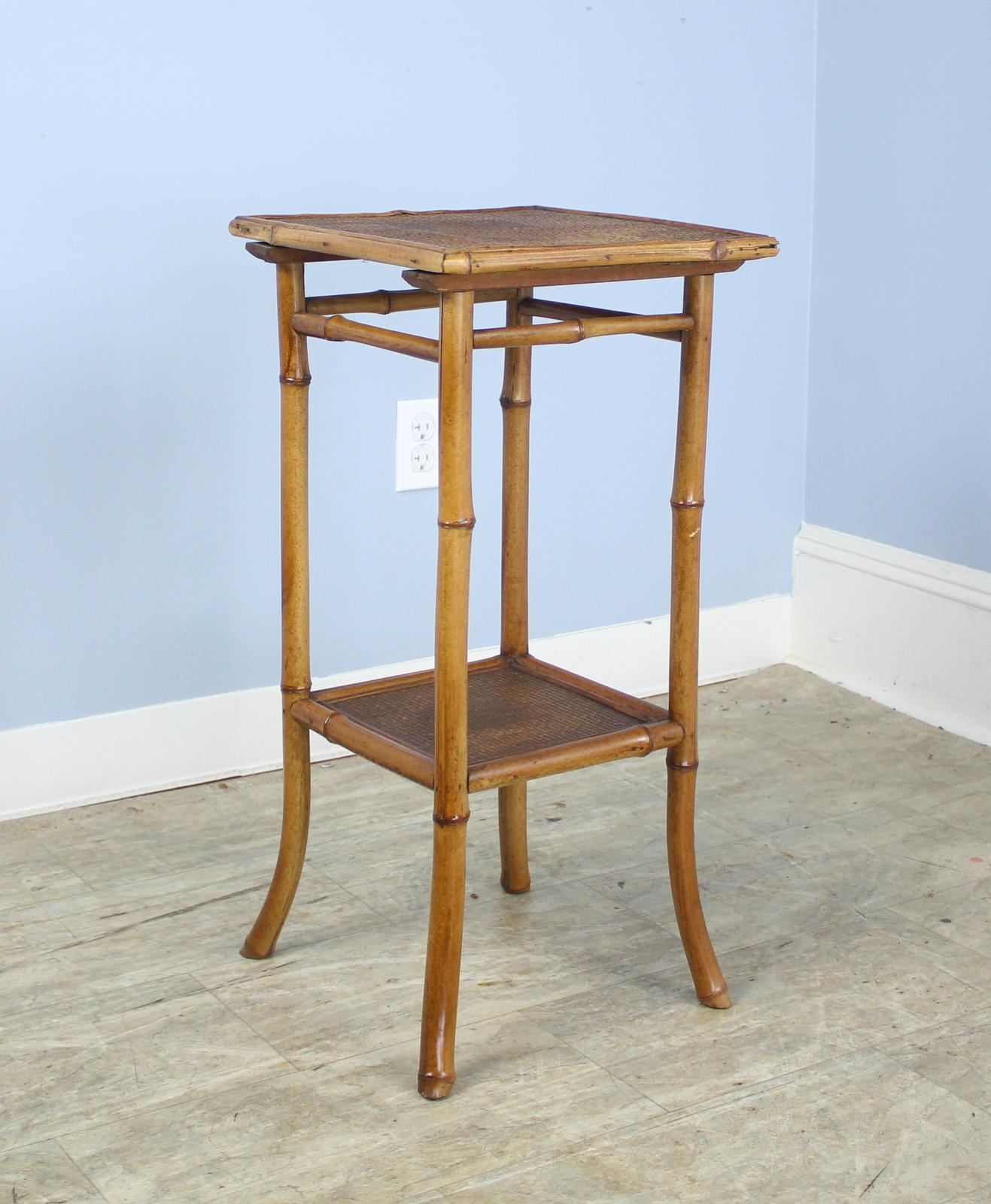 An antique English bamboo side table, with flared legs and with two shelves. Both shelves are made of tightly woven rattan that is in good condition. The bamboo is in good sturdy condition. Charming as an end or lamp table.