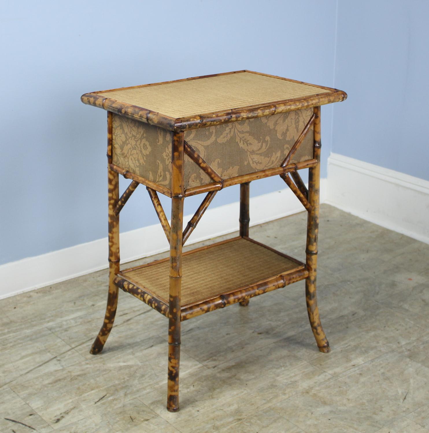 An attractive antique bamboo side table, originally a sewing box on flared legs. The box lifts from one hinged side, and has a floral motif on the side. A delicate and charming side table or end table.