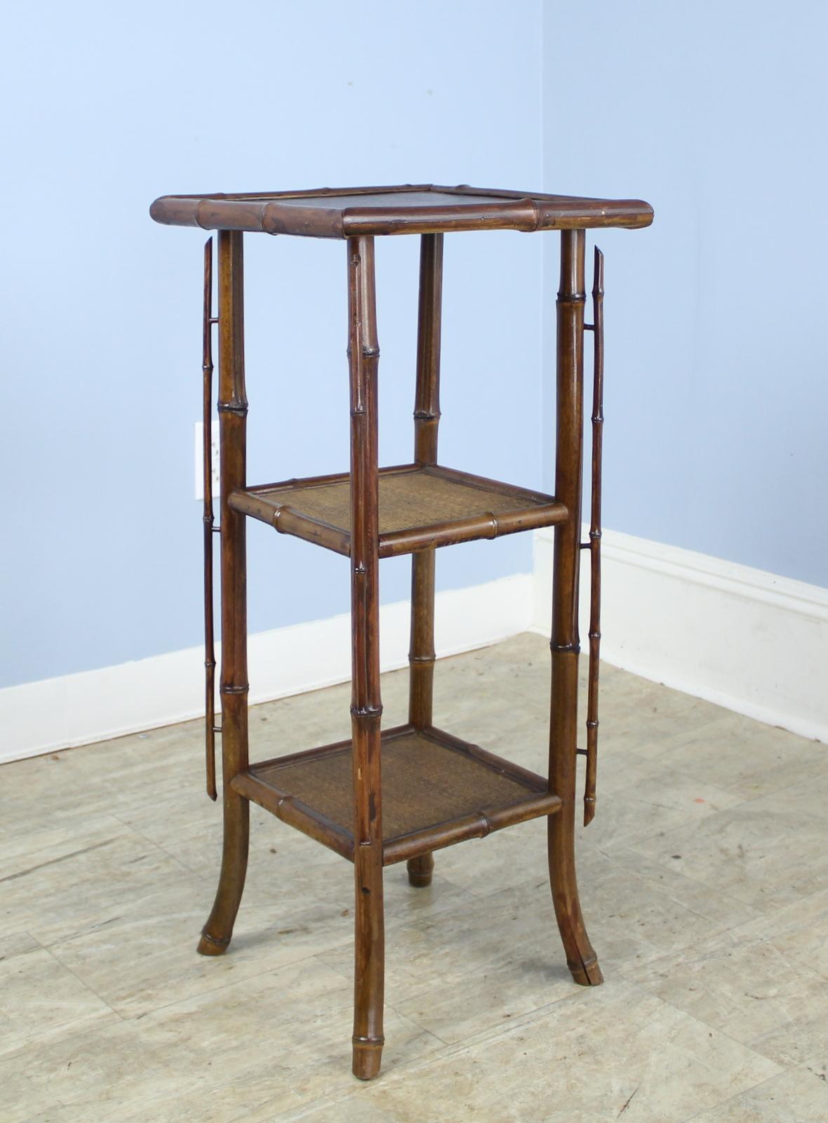 An antique English bamboo side table, with flared legs accented with vertical detail and its original leather top,. The two bottom shelves are made of tightly woven rattan that is in very good condition. The top has a stylish leather surface. The