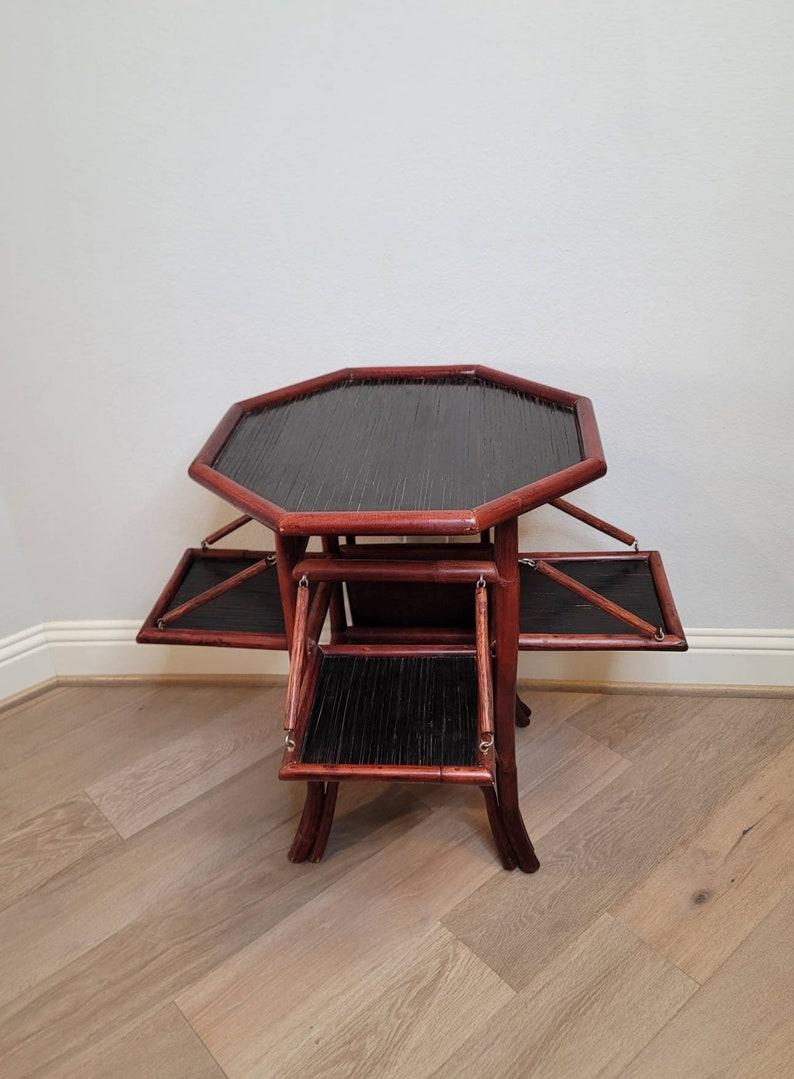 A three tier bamboo dessert server or tea table from the late 19th to early 20th century. Likely English, having an octagonal shaped black lacquered top and square central lower tier, framed in oxblood red stained bamboo, featuring four folding