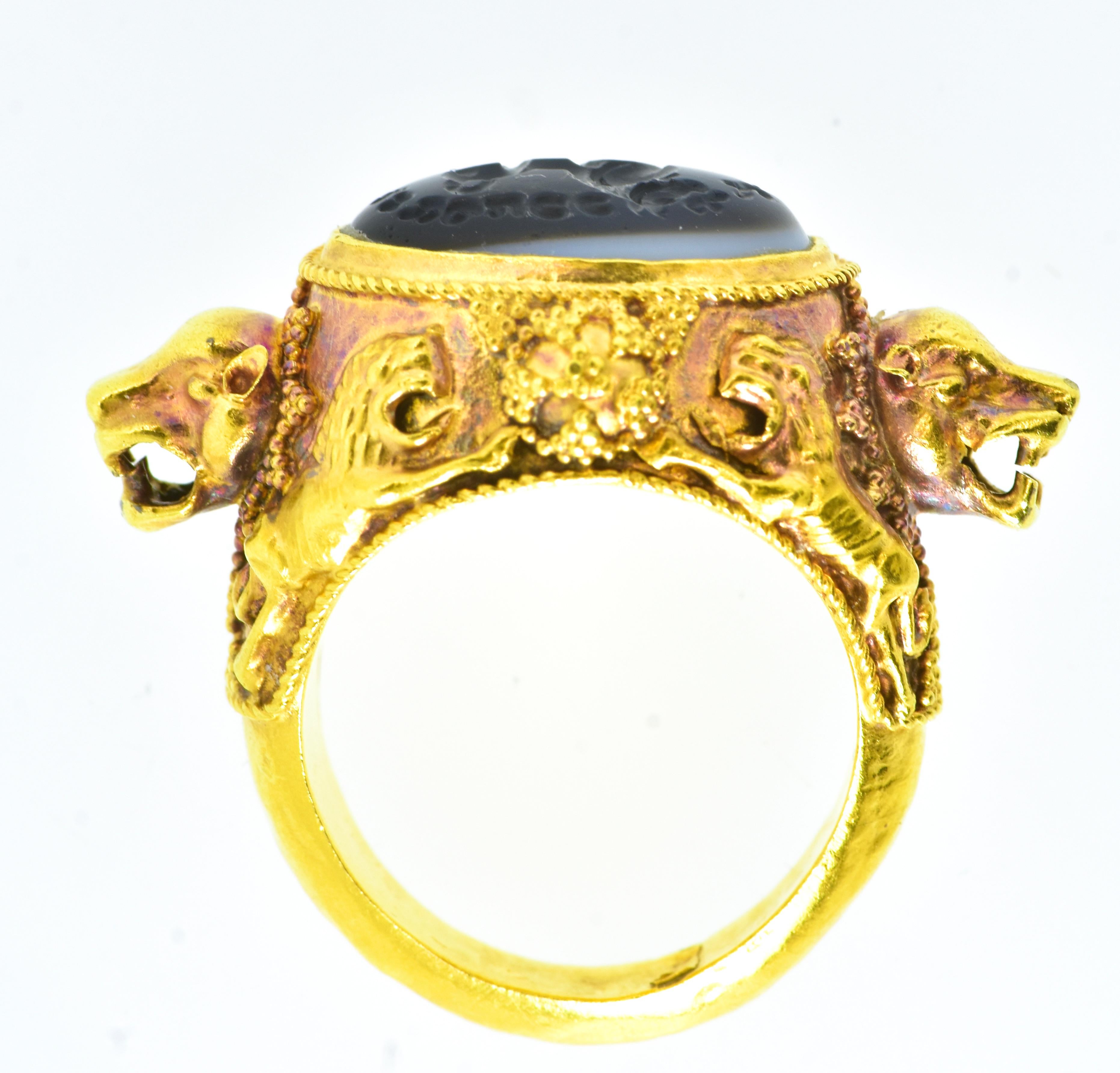 Antique intaglio carved in banded agate in an ornate 18K yellow gold ring.  The  center carving, probably Roman, is of a striding lion.  There appears to be an ancient writing on the periphery of the stone which we cannot decipher.
On each shoulder