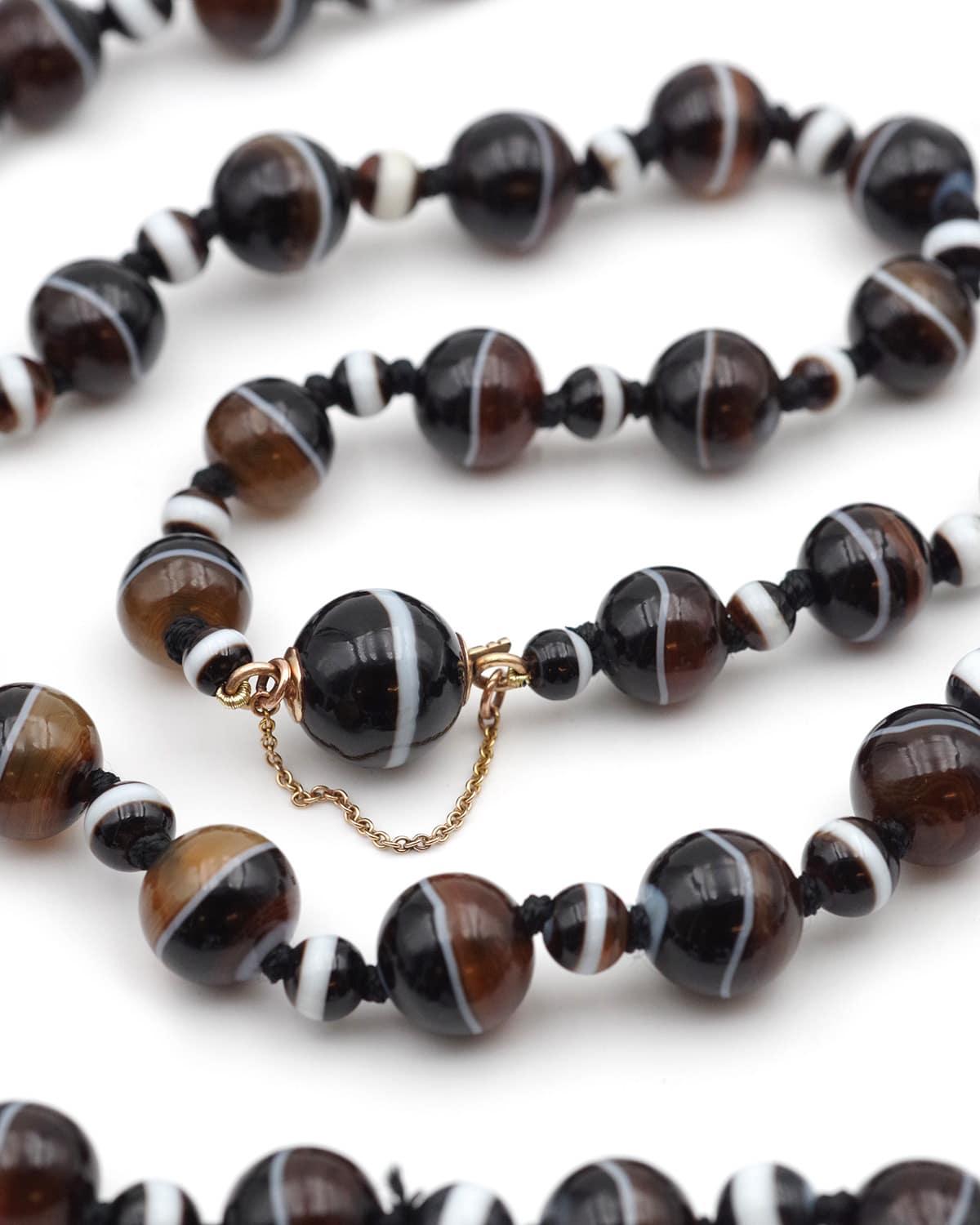 Antique banded agate necklace with its 14 karat gold clasp. Long necklace composed of 95 banded agate beads. The beads are arranged in a cascade, alternating between small and large beads. The clasp is hidden in a bead of the necklace and secured